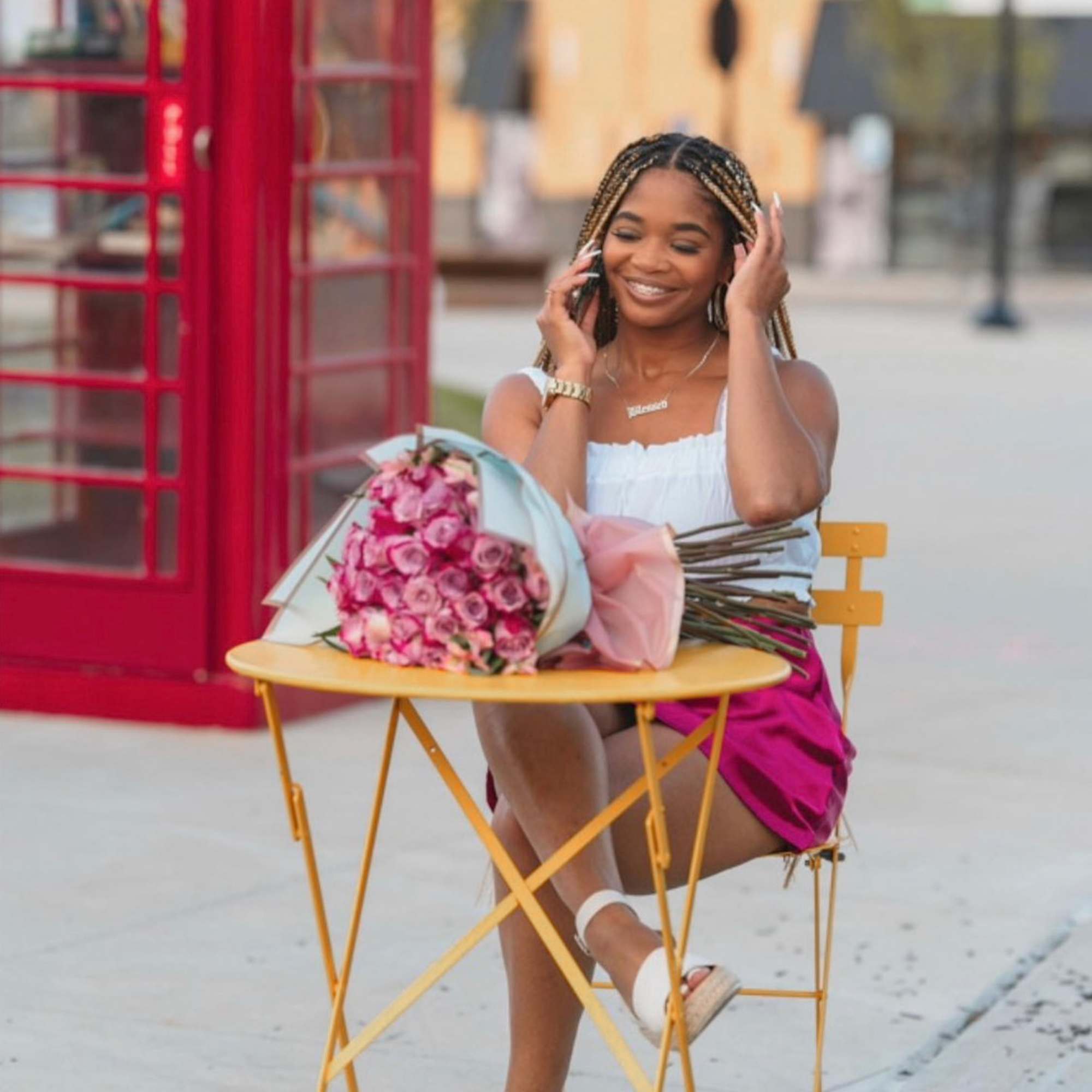 Woman seated beside a bouquet of pink roses on a small table