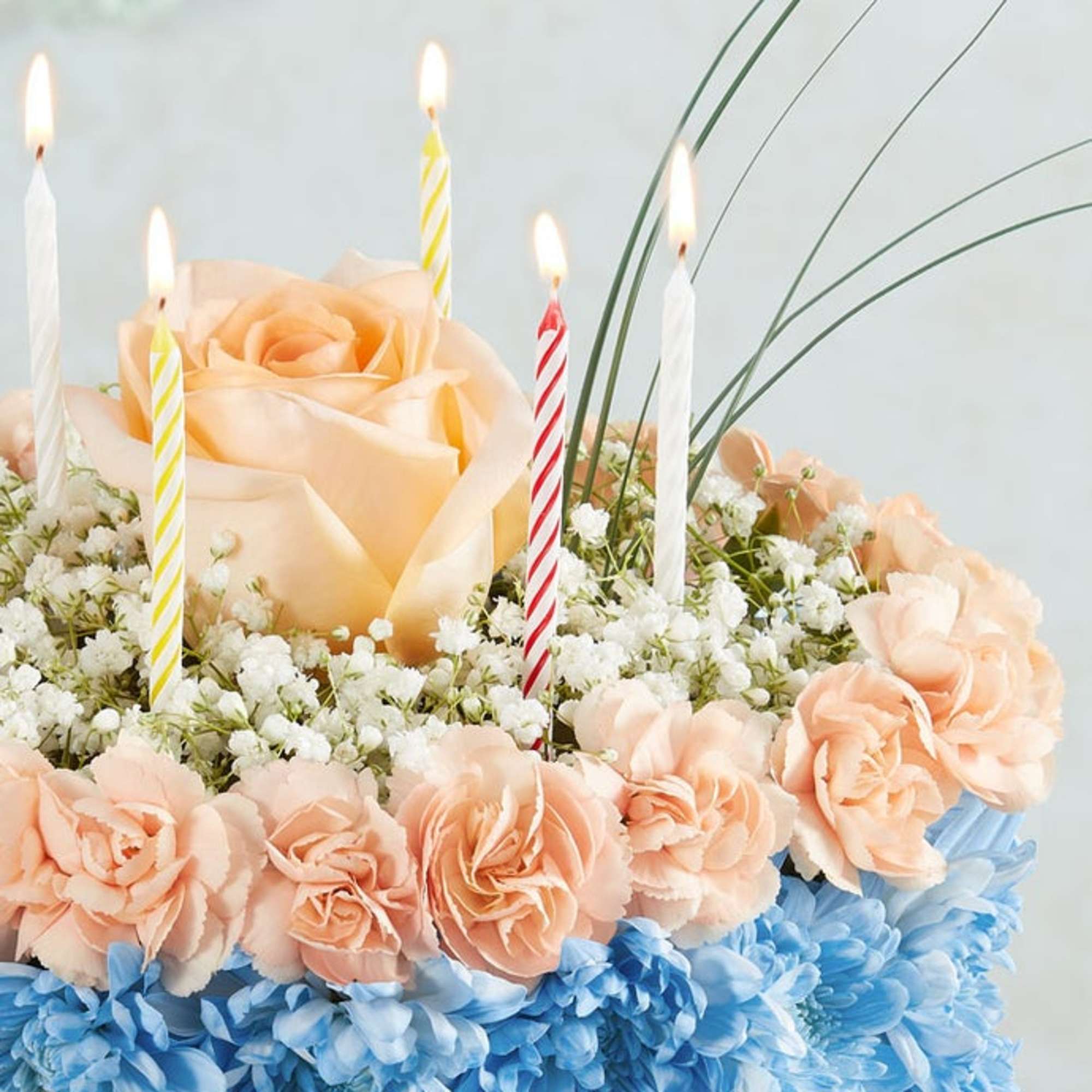 Peach roses with blue and white flowers and lit striped candles