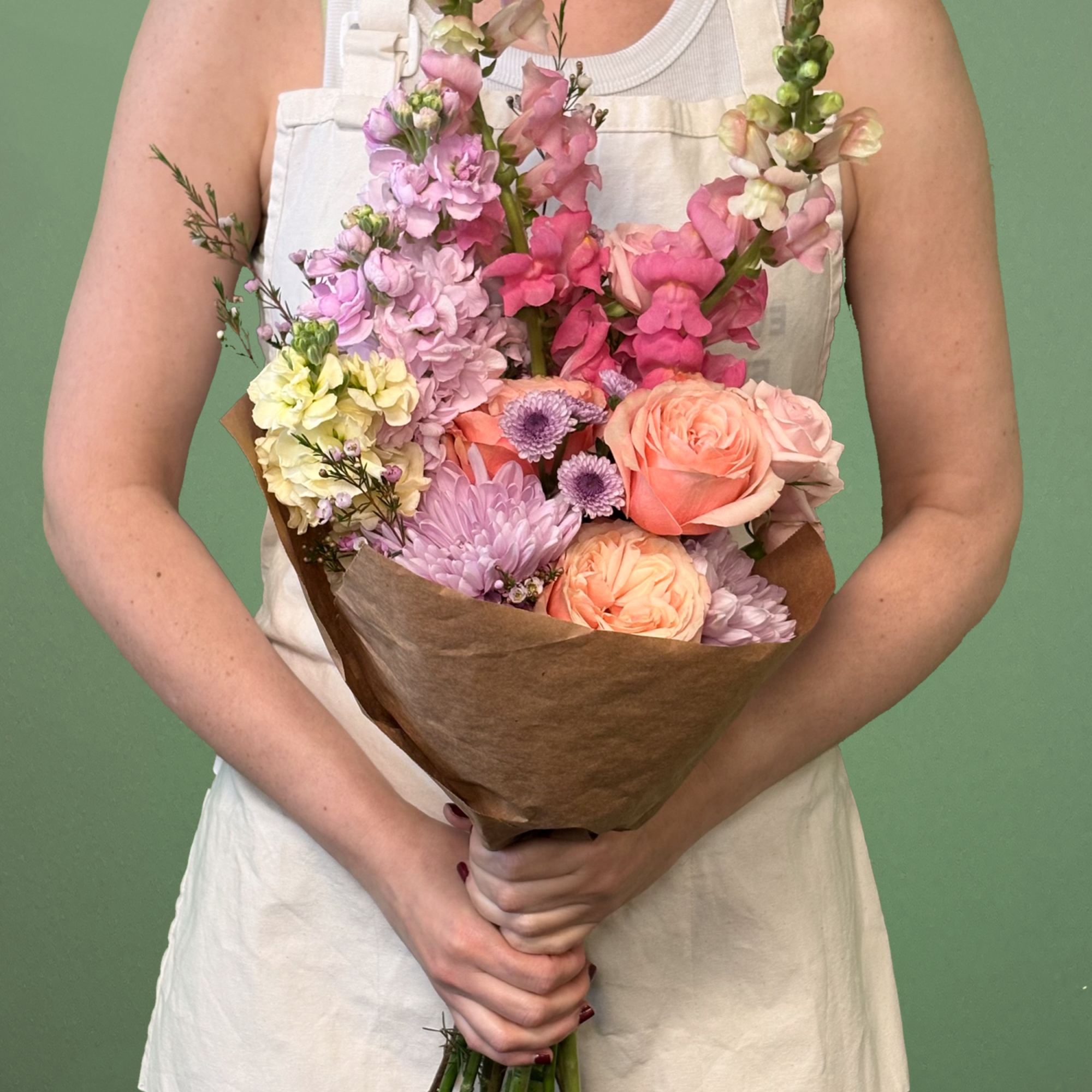 Handheld bouquet of pink, peach, and lavender flowers wrapped in brown paper