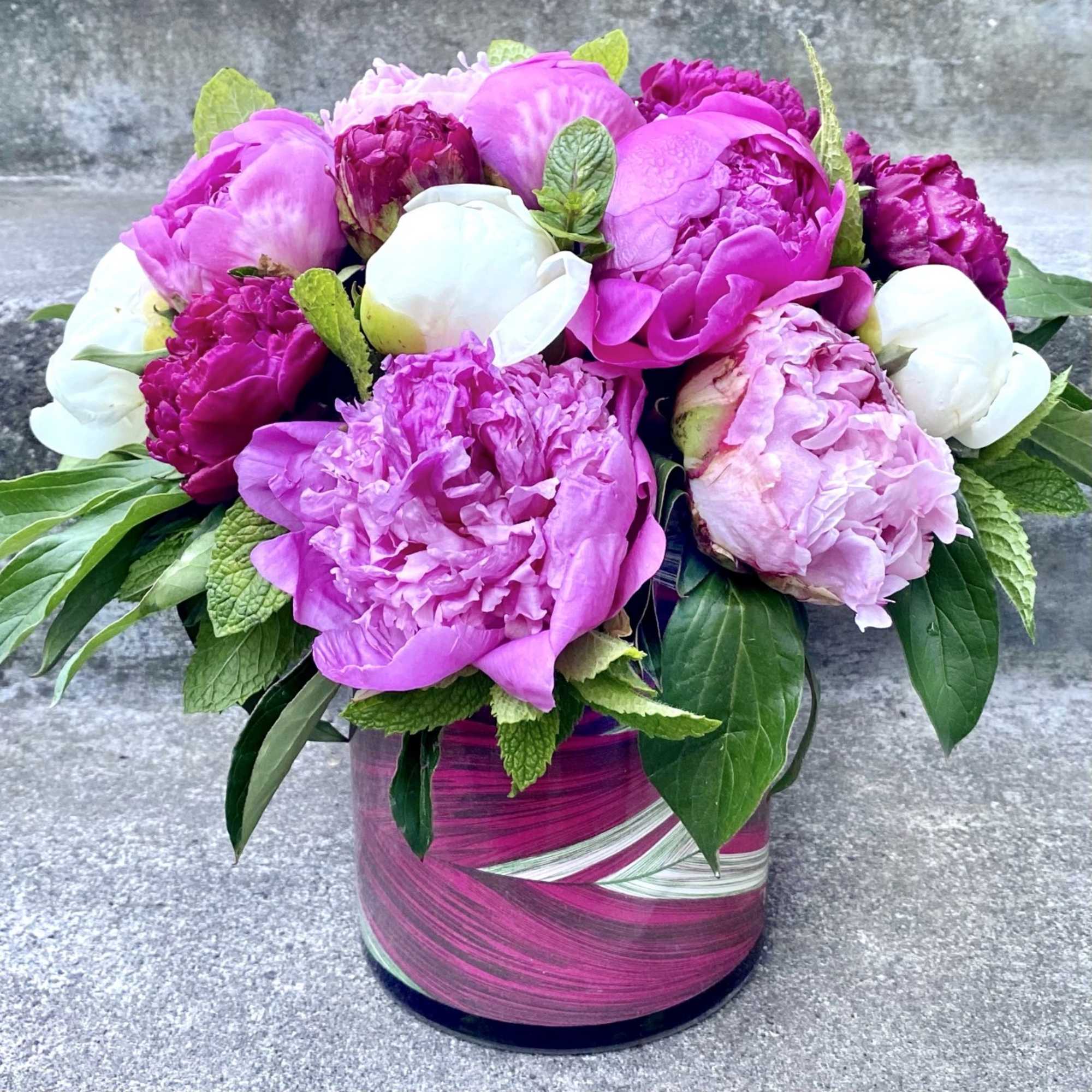 Pink and white peonies arranged in a magenta glass vase
