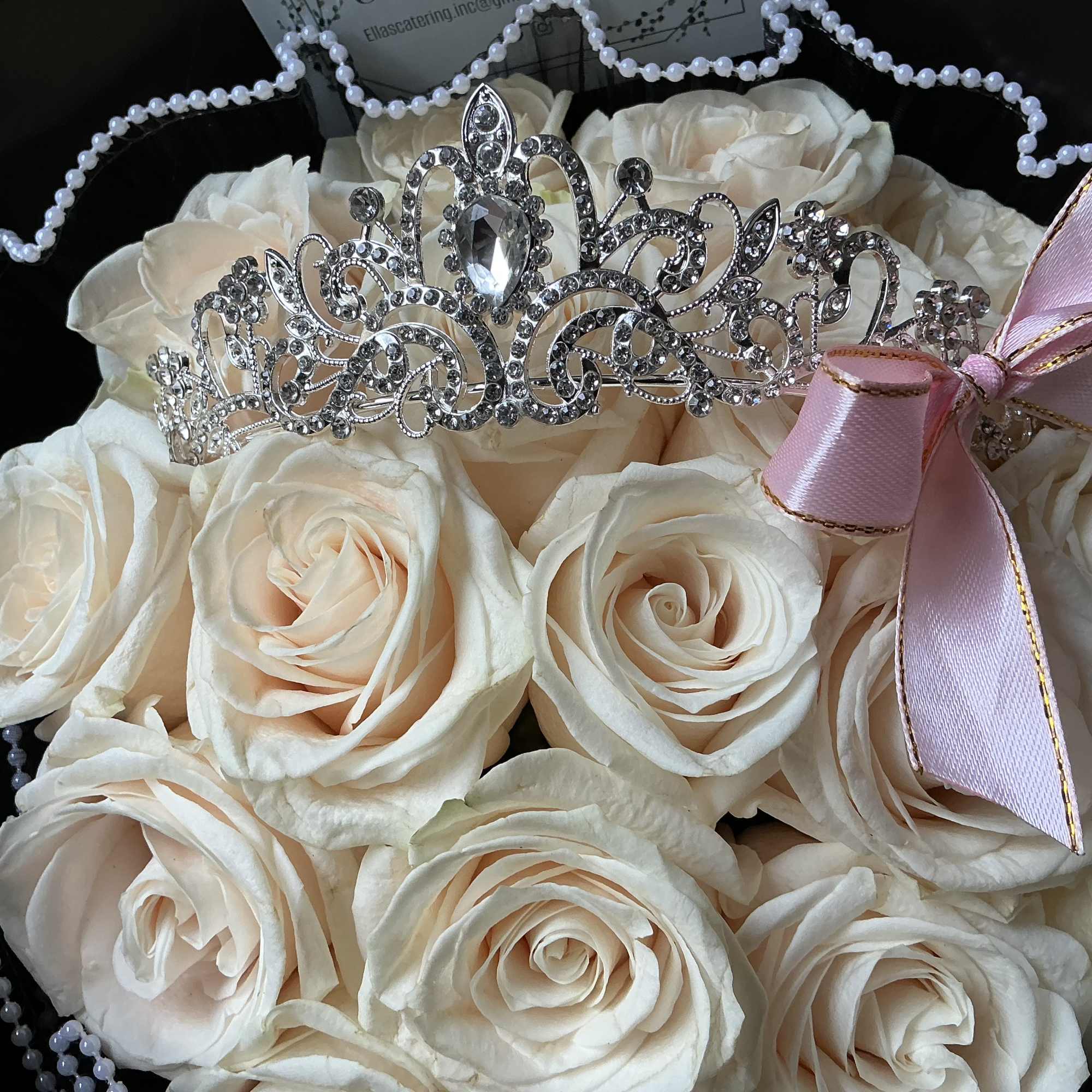 Cream roses arranged with a jeweled tiara and pink ribbon