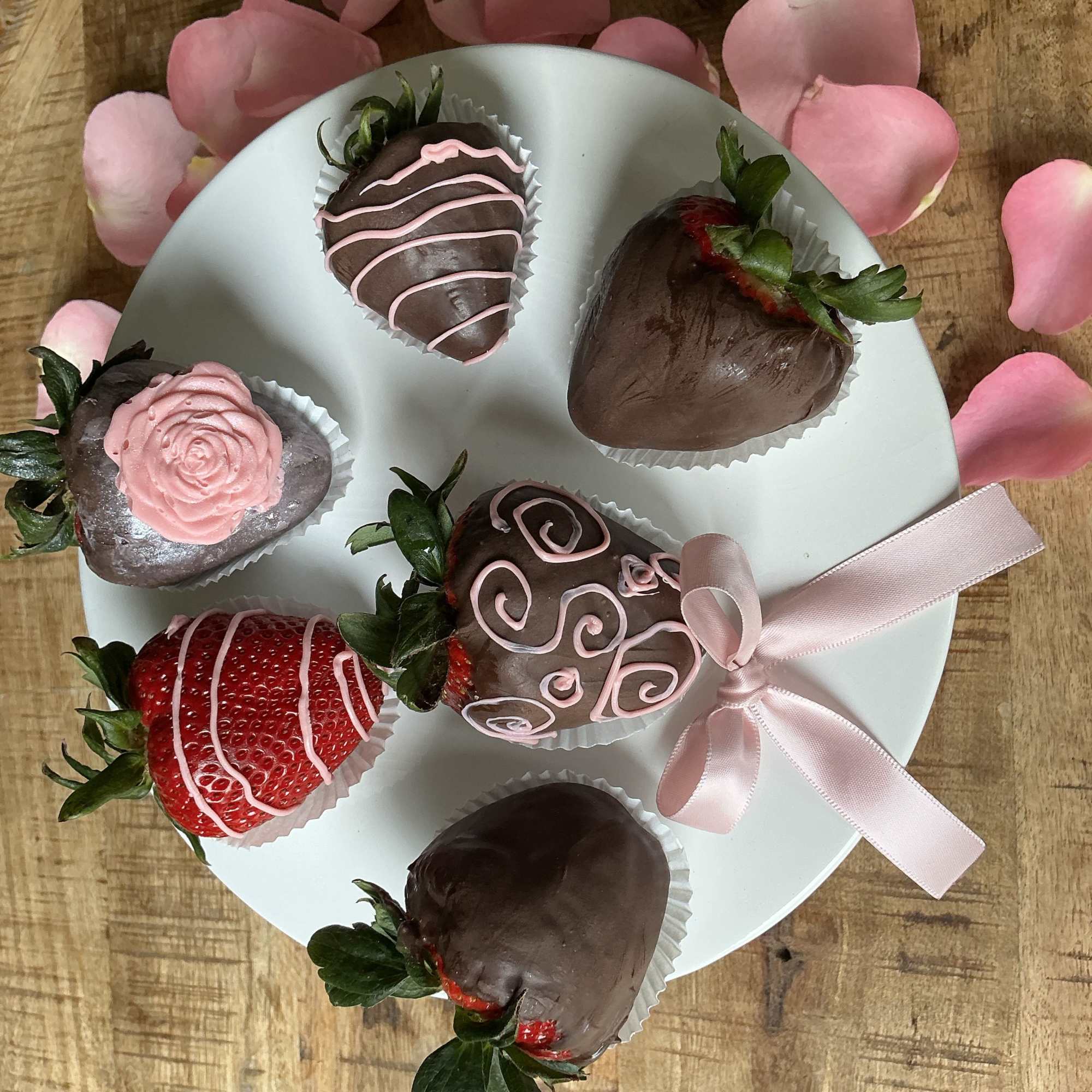 Chocolate-covered strawberries on a white plate with pink ribbon and petals