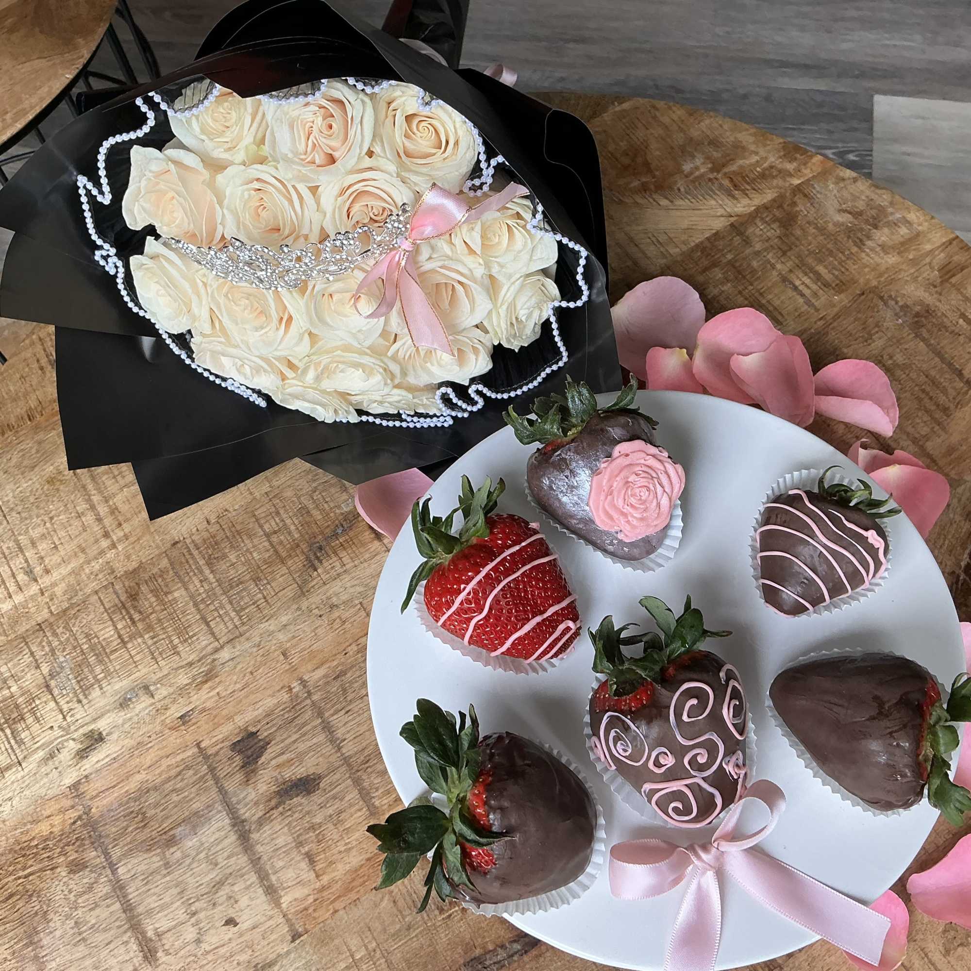 Cream rose bouquet with black wrapping beside chocolate-covered strawberries on a plate