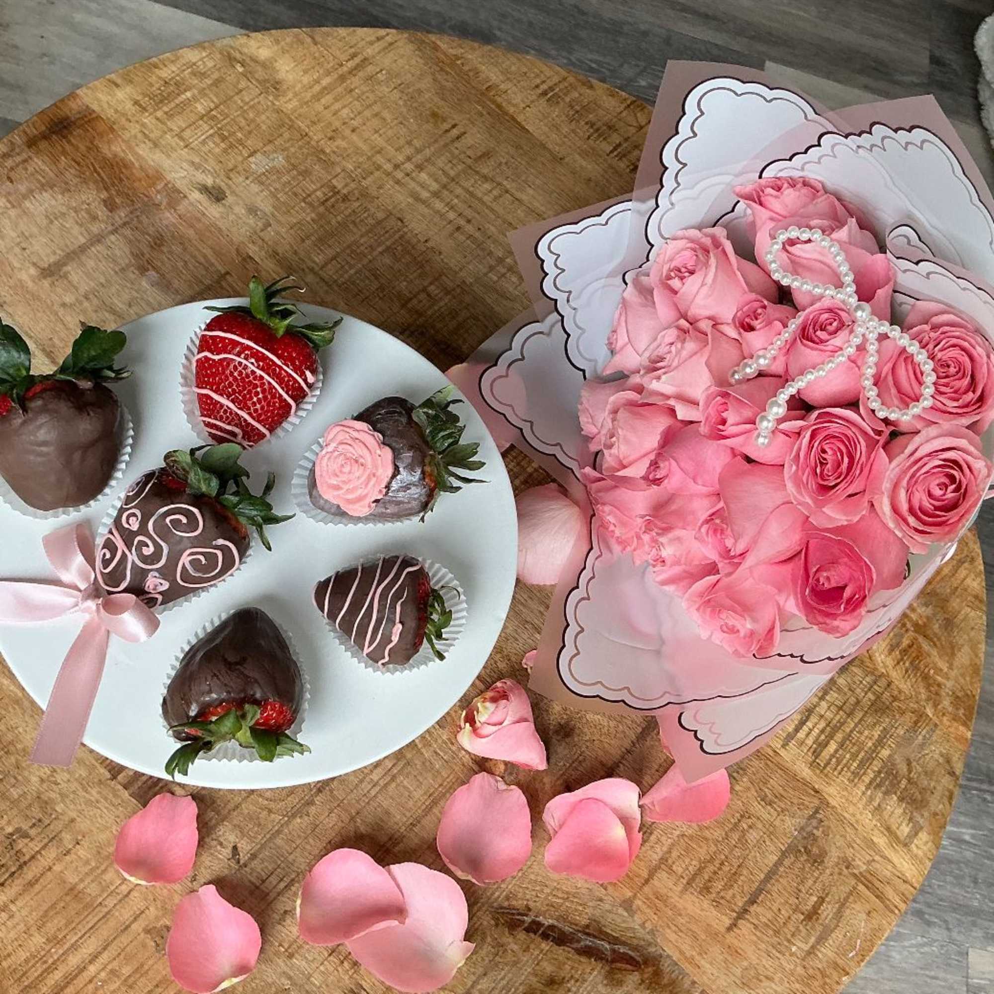 Pink rose bouquet with pearl accents beside chocolate-covered strawberries on a plate