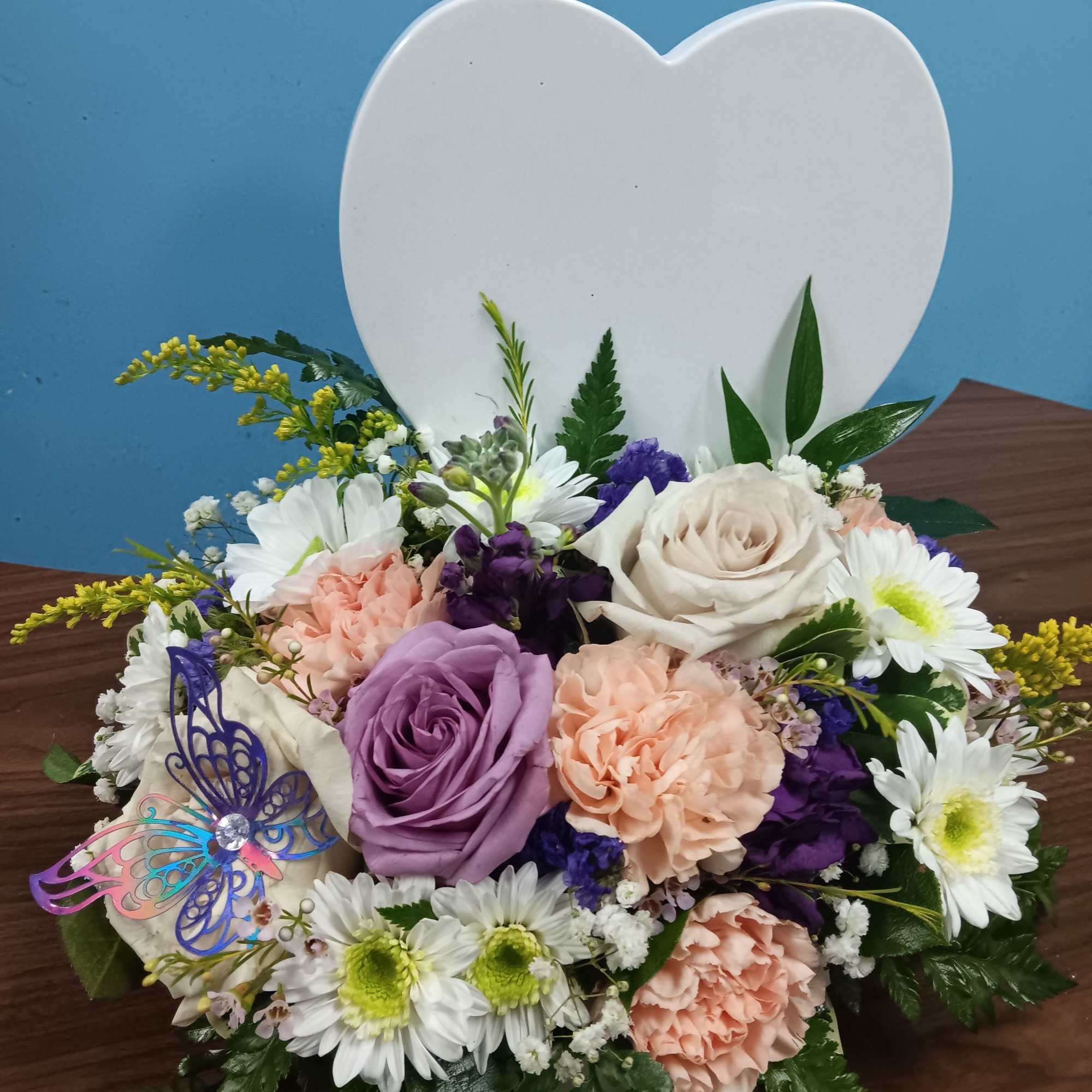 Creamy roses and soft lavender blooms nestle against a white heart-shaped plaque