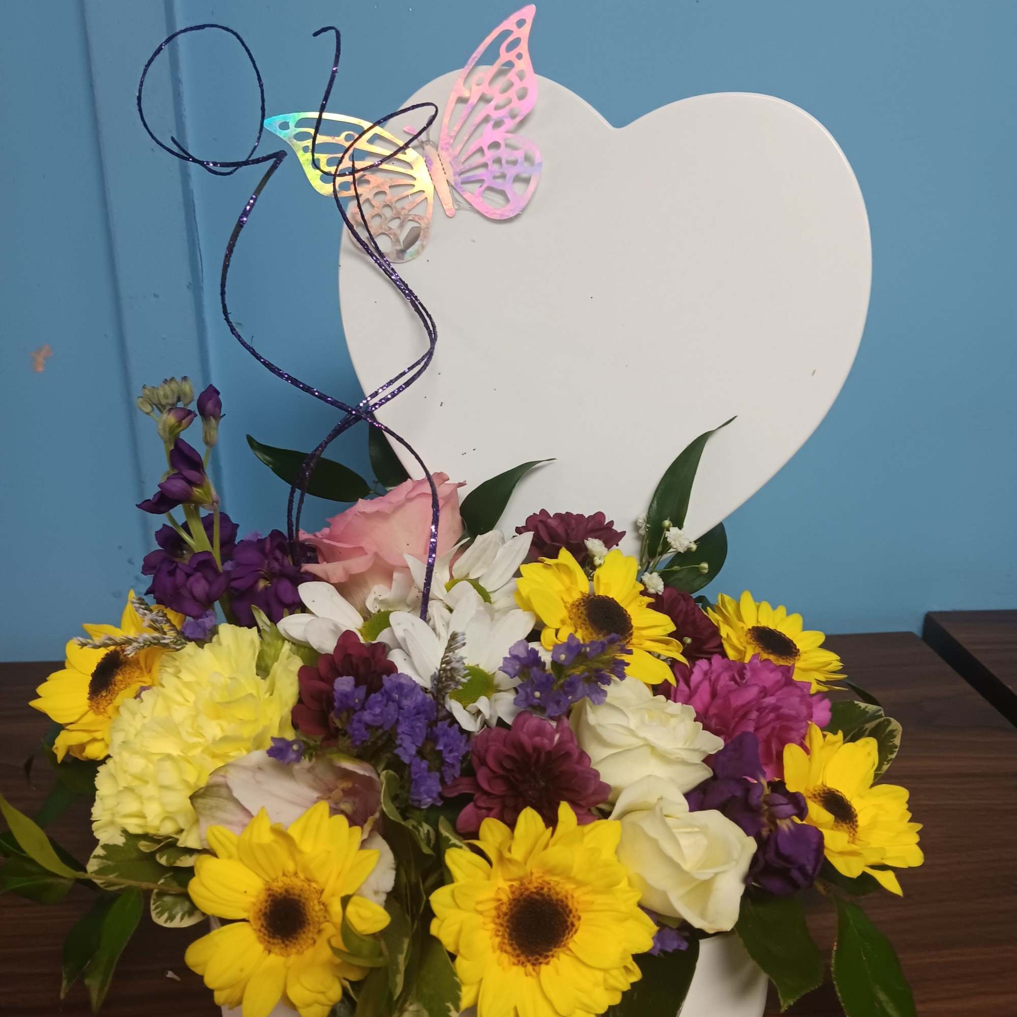 Creamy roses and soft lavender blooms nestle against a white heart-shaped plaque