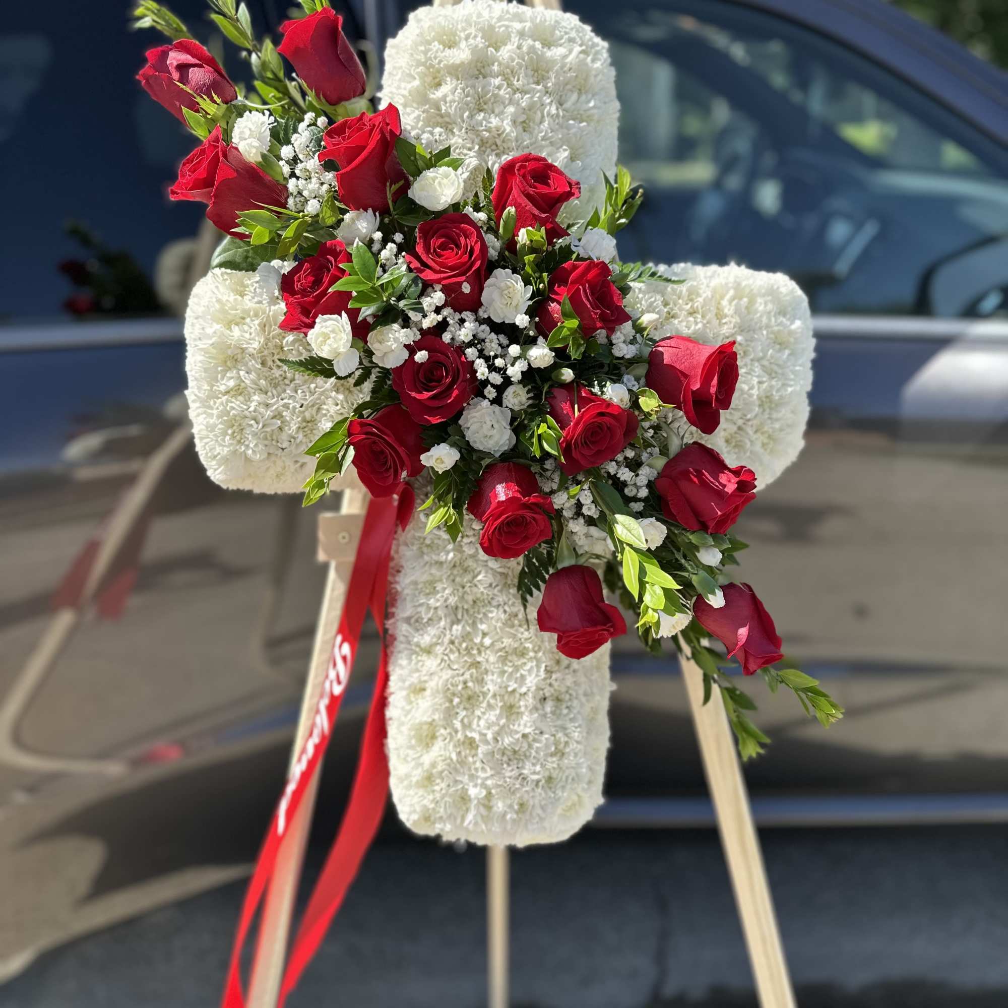 Red roses arranged on a white floral cross on an easel