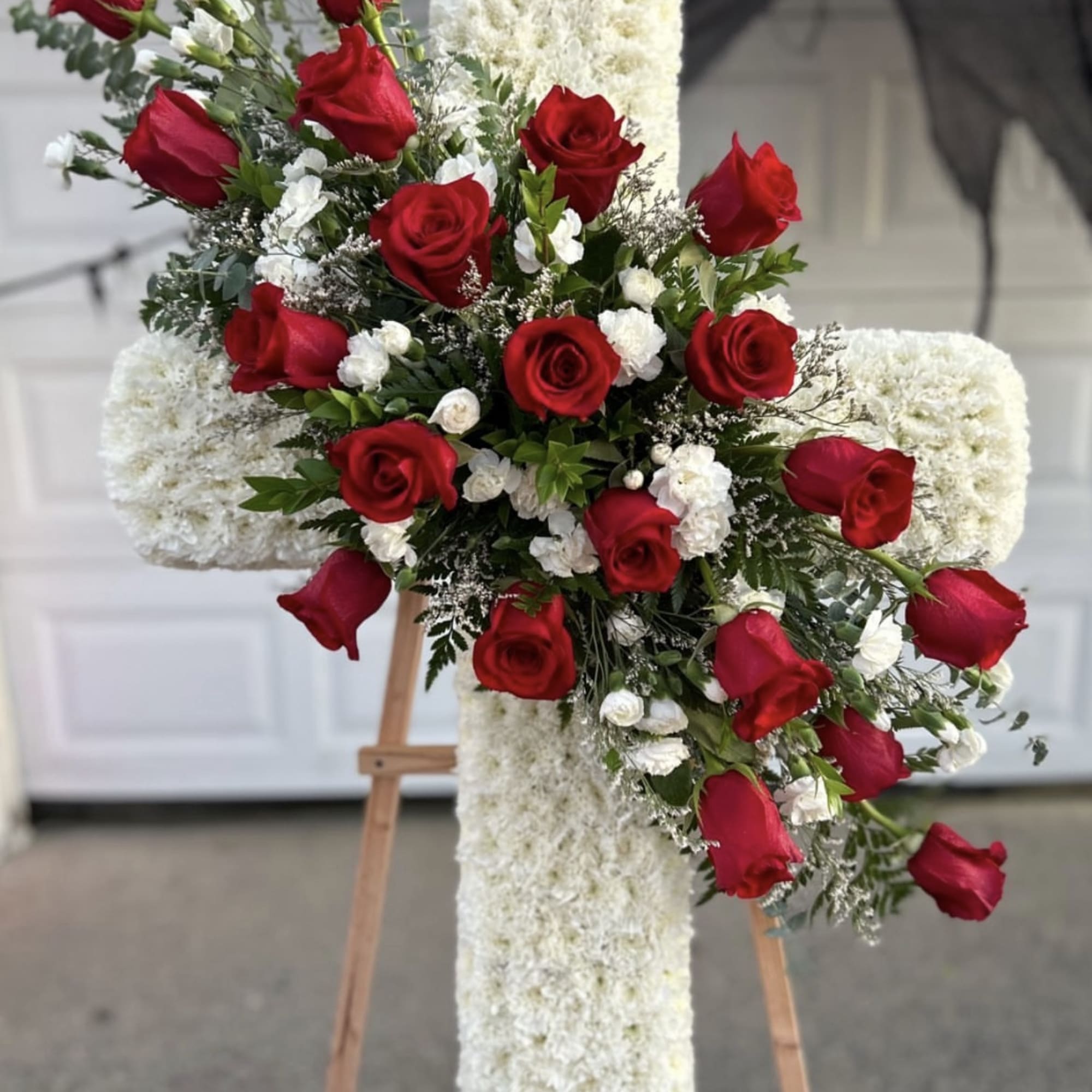 Red roses arranged on a white floral cross on an easel