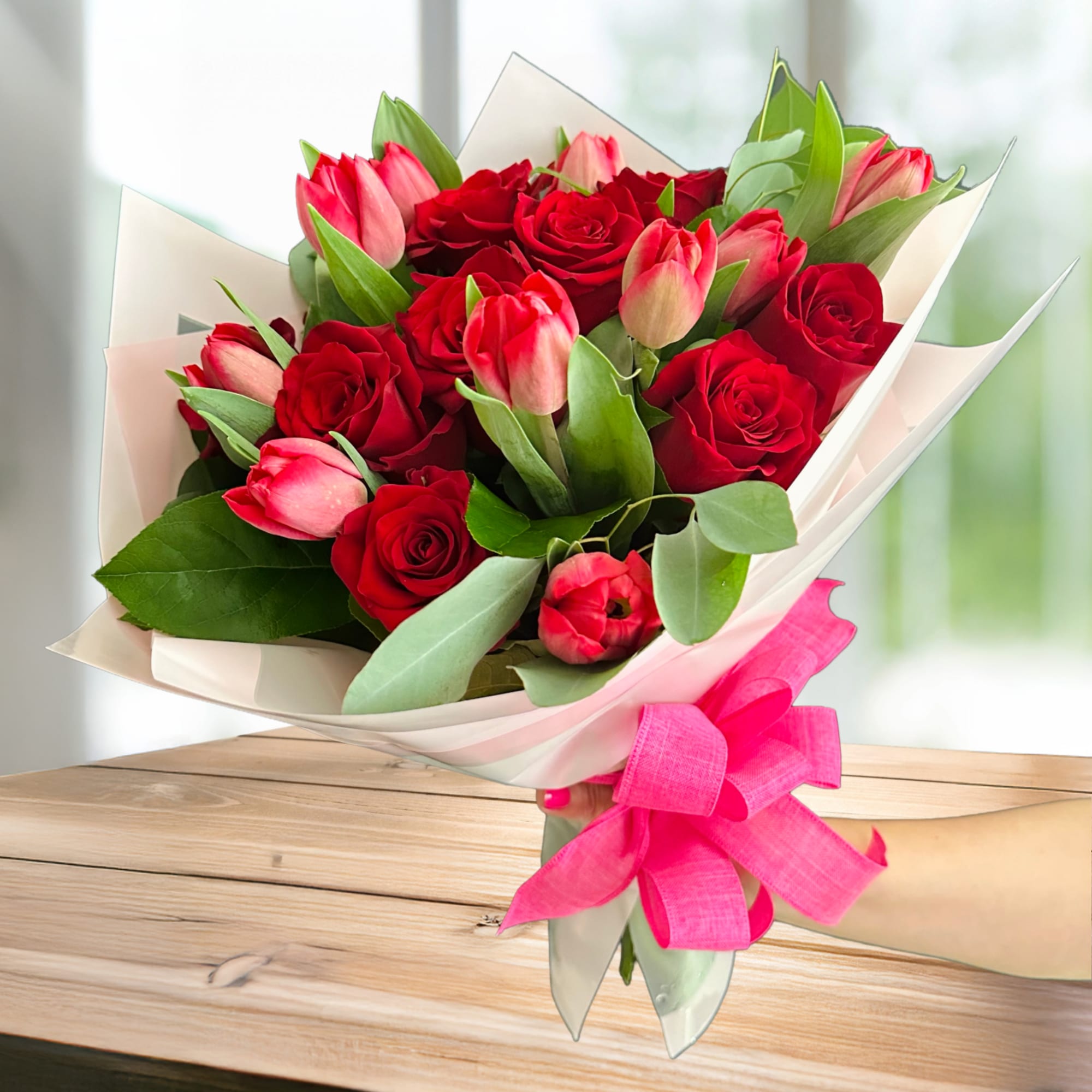 Bouquet of red roses and pink tulips wrapped in white paper with a pink ribbon