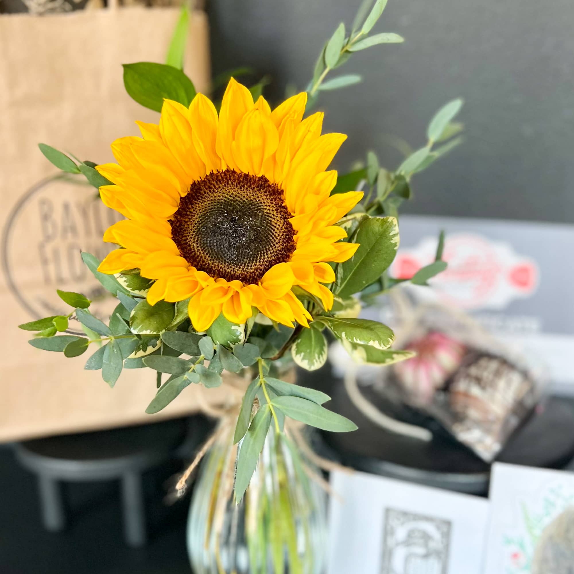 Single sunflower bouquet in a glass vase with greenery