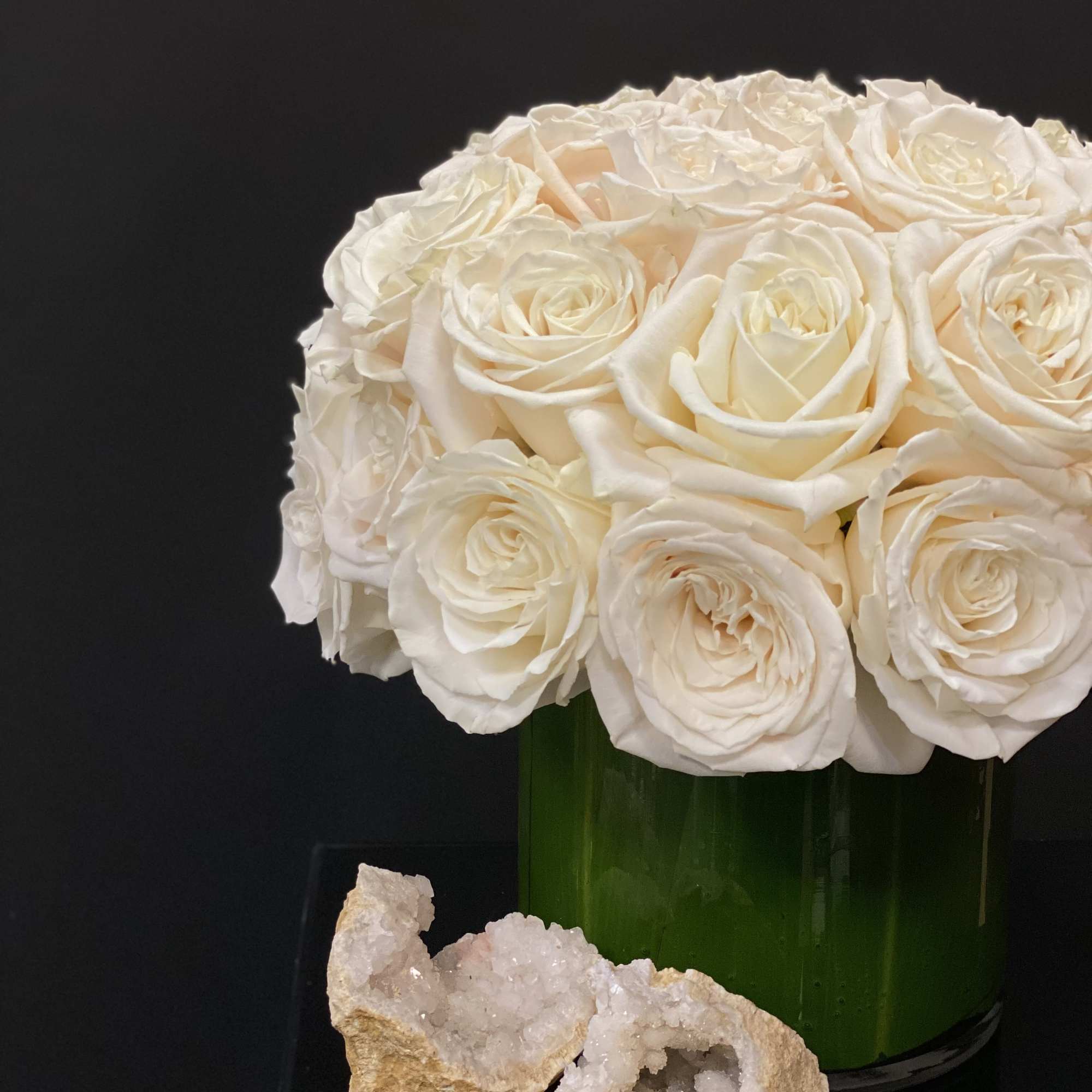 White roses arranged in a green glass vase with two crystal geodes in front