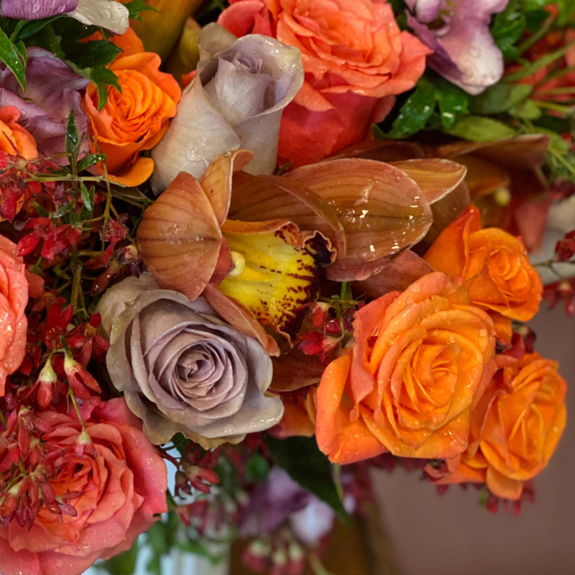 Bouquet of orange and lavender roses with orchids and tropical blooms