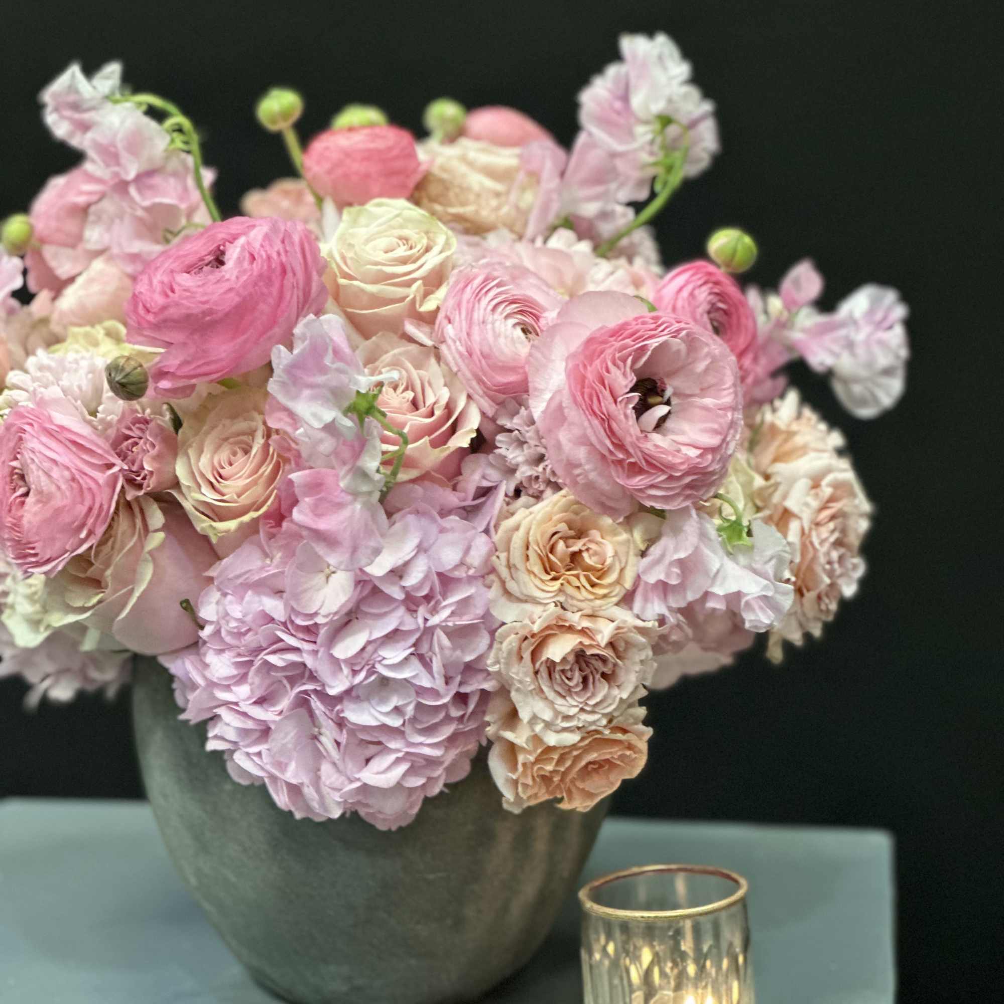 Pink and peach flowers arranged in a gray vase beside a small candle holder