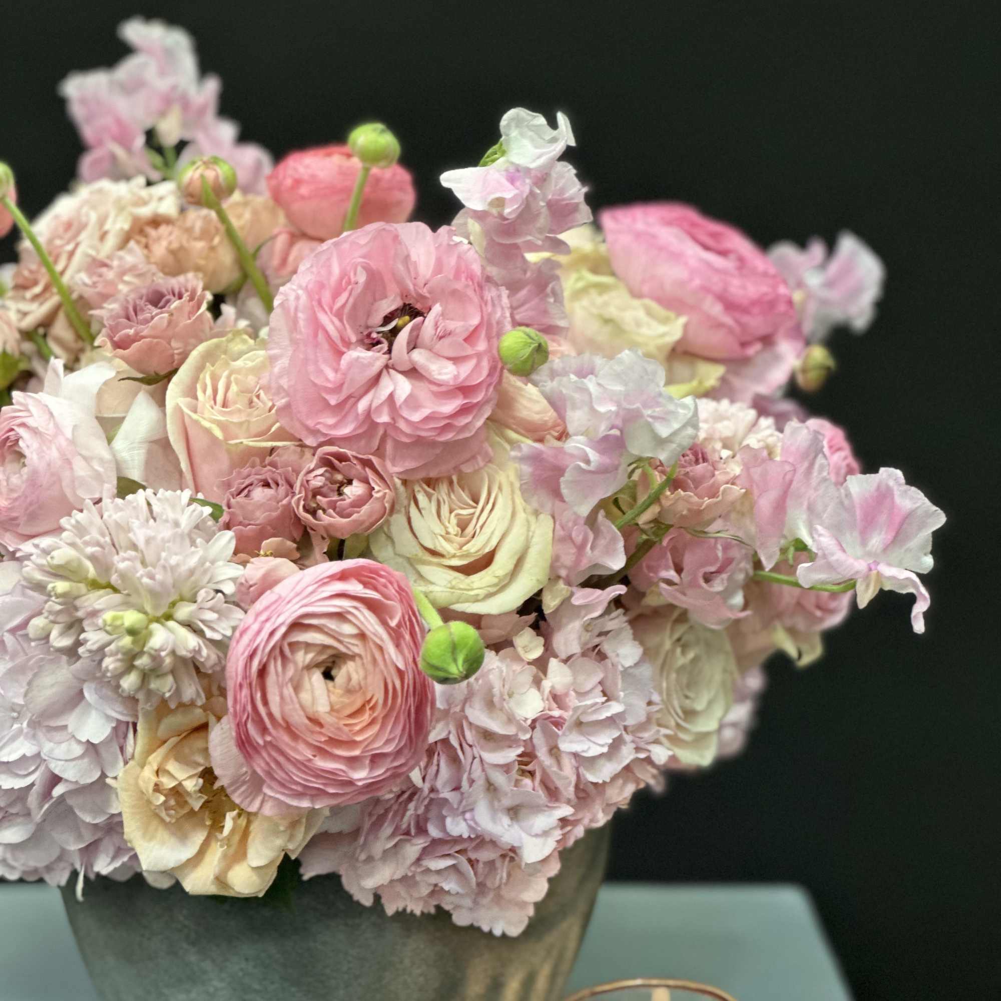 Pink and cream floral arrangement in a gray vase with a candle nearby