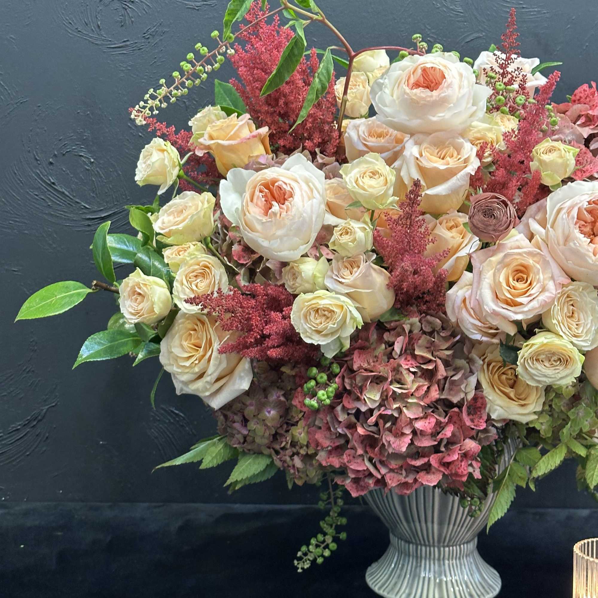 This stunning arrangement showcases peach garden roses, lush hydrangeas, and delicate spray