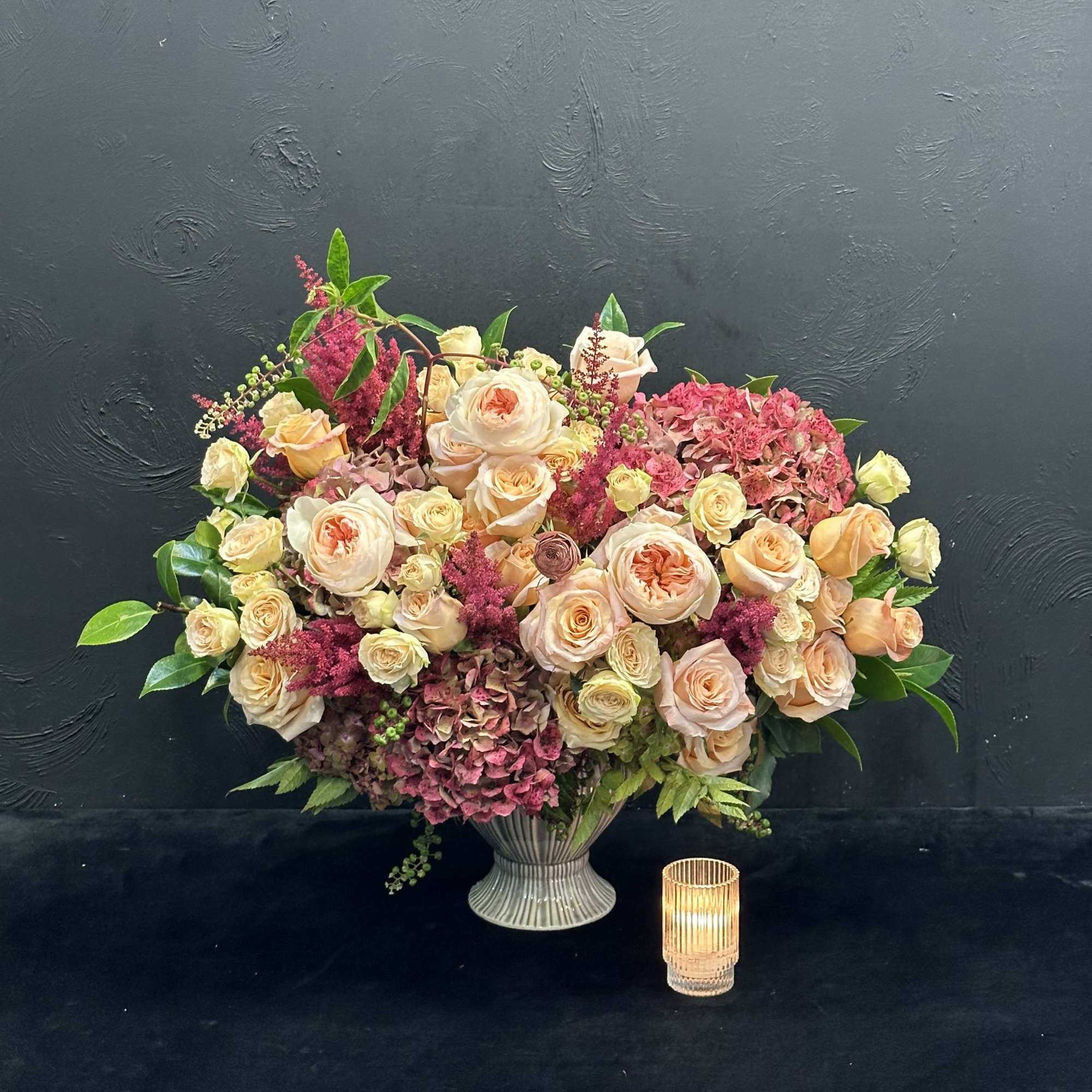 This stunning arrangement showcases peach garden roses, lush hydrangeas, and delicate spray