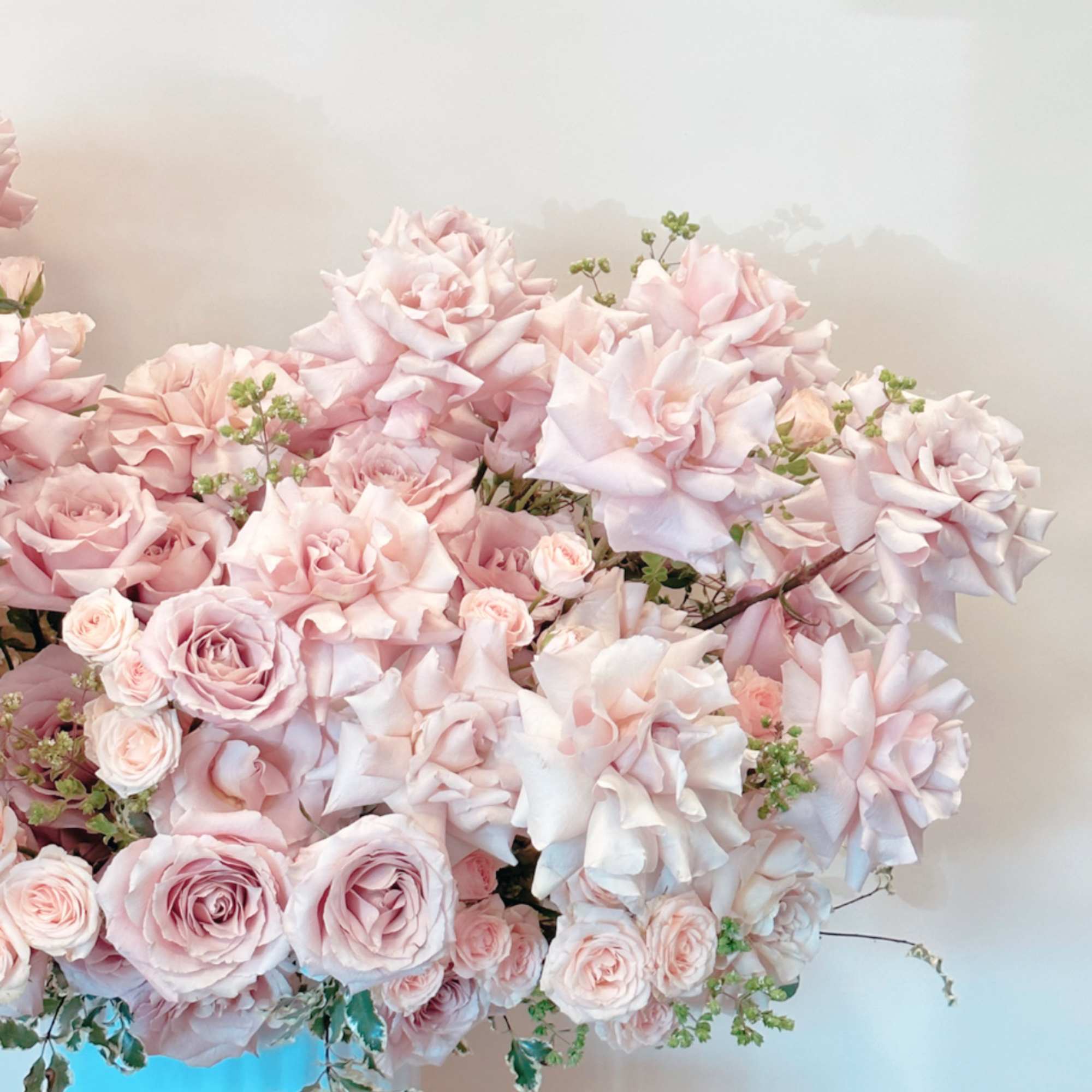 Large pale pink rose arrangement in a blue container with a glass candle holder
