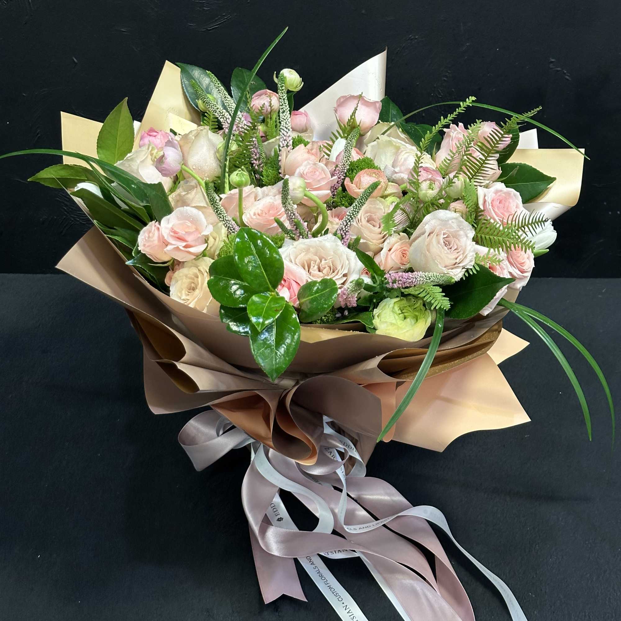 Bouquet of pale pink and white roses wrapped in brown paper with ribbons