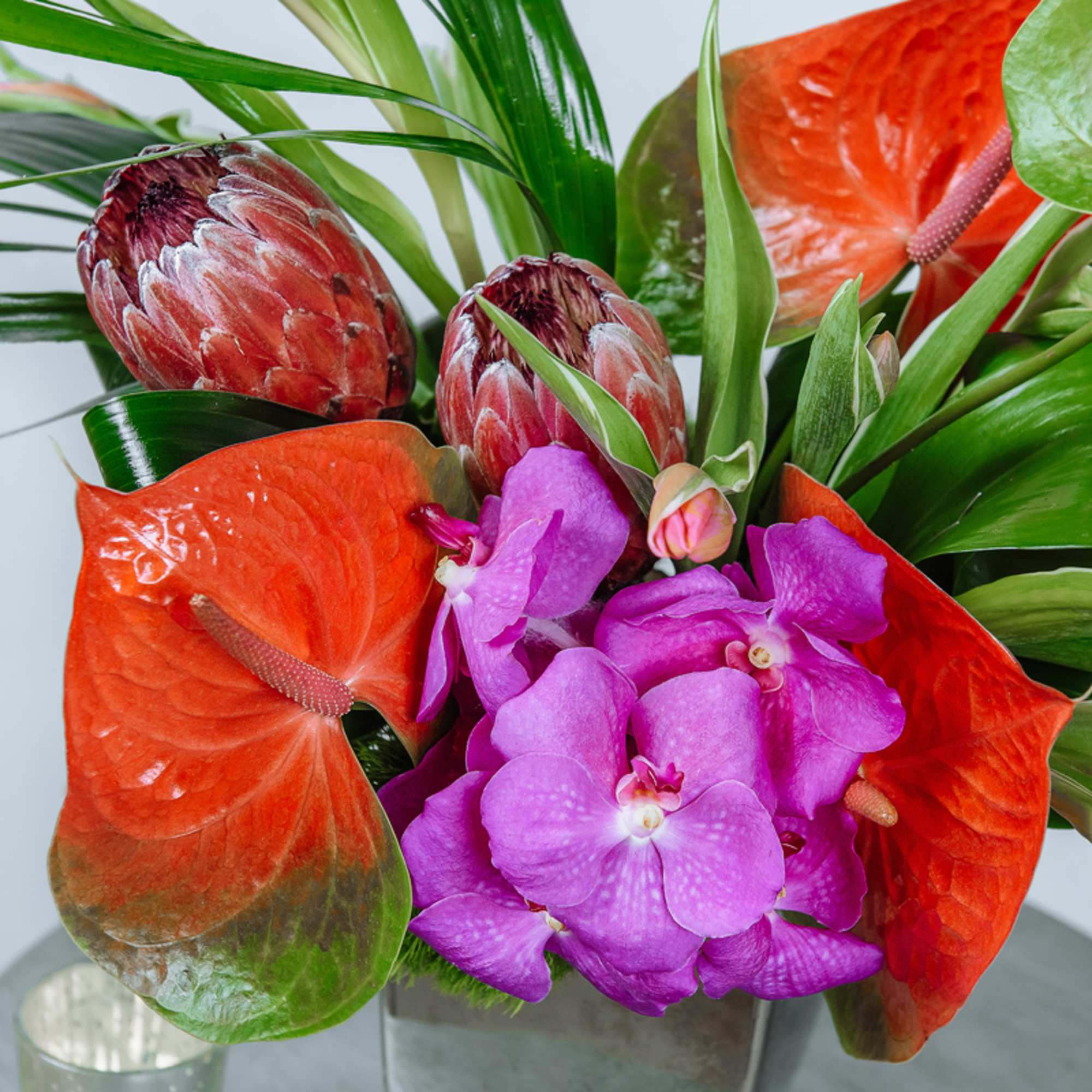 Tropical bouquet with orange anthuriums and purple orchids in a vase