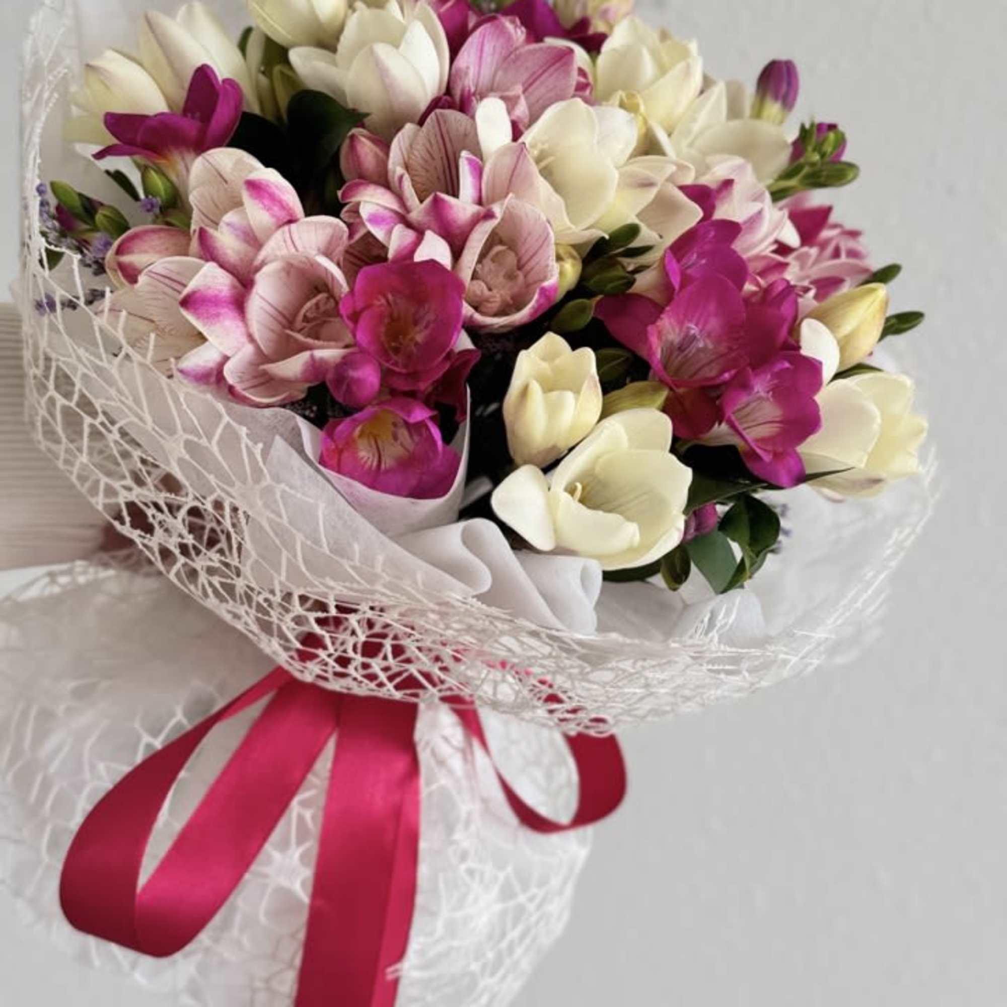 Bouquet of pink and white flowers wrapped in white mesh with a pink ribbon