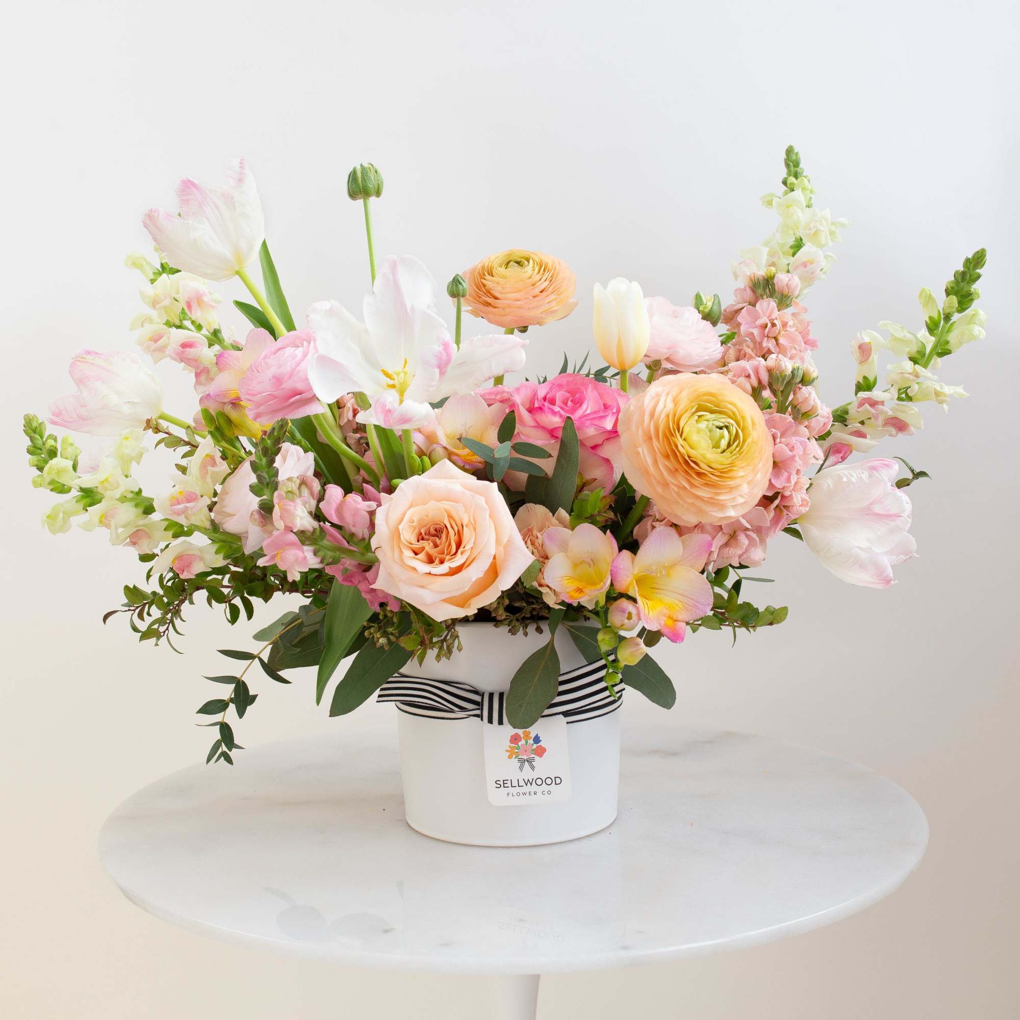 Pastel flower arrangement in a white hatbox with a striped ribbon