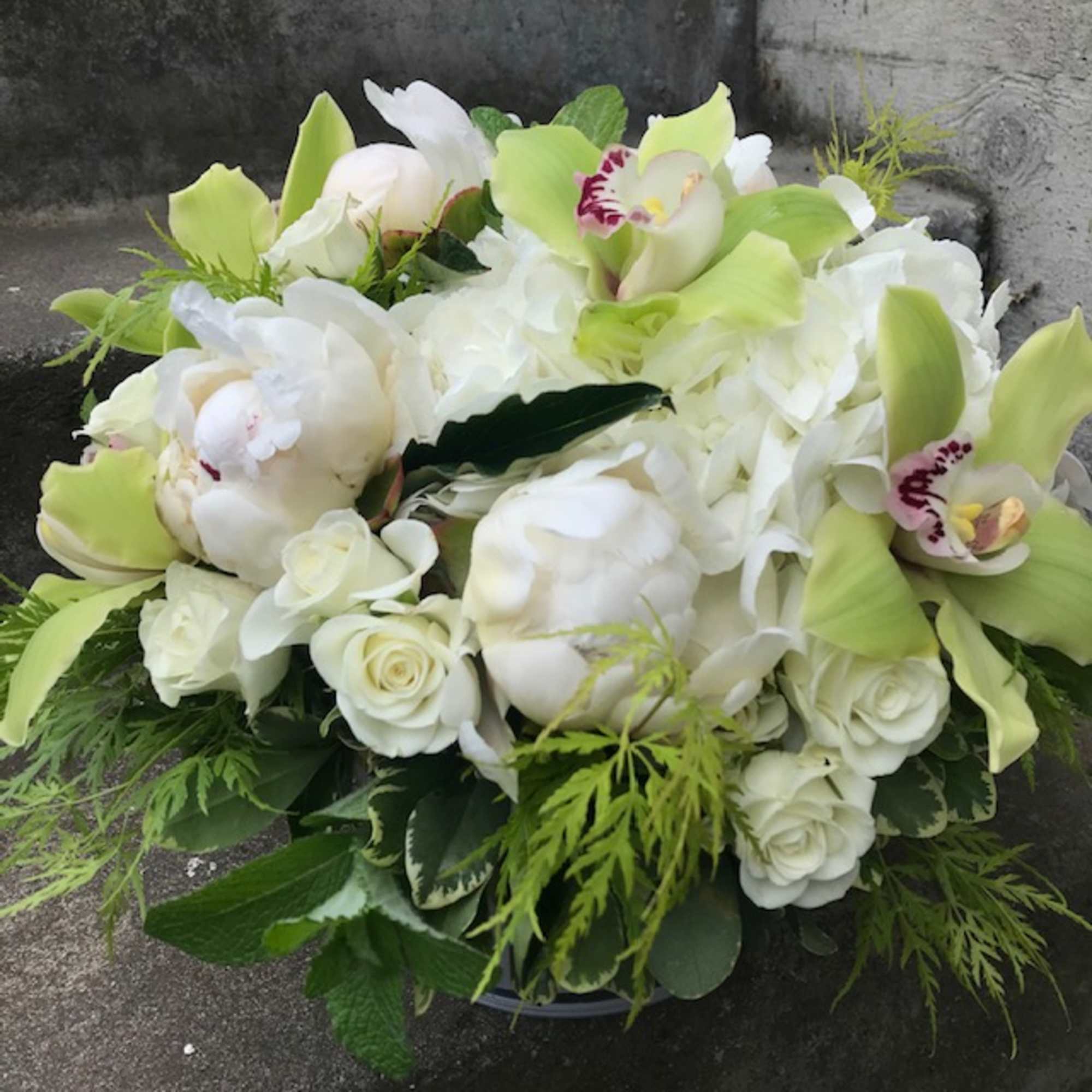 White and pale green floral arrangement with orchids and roses in a low container