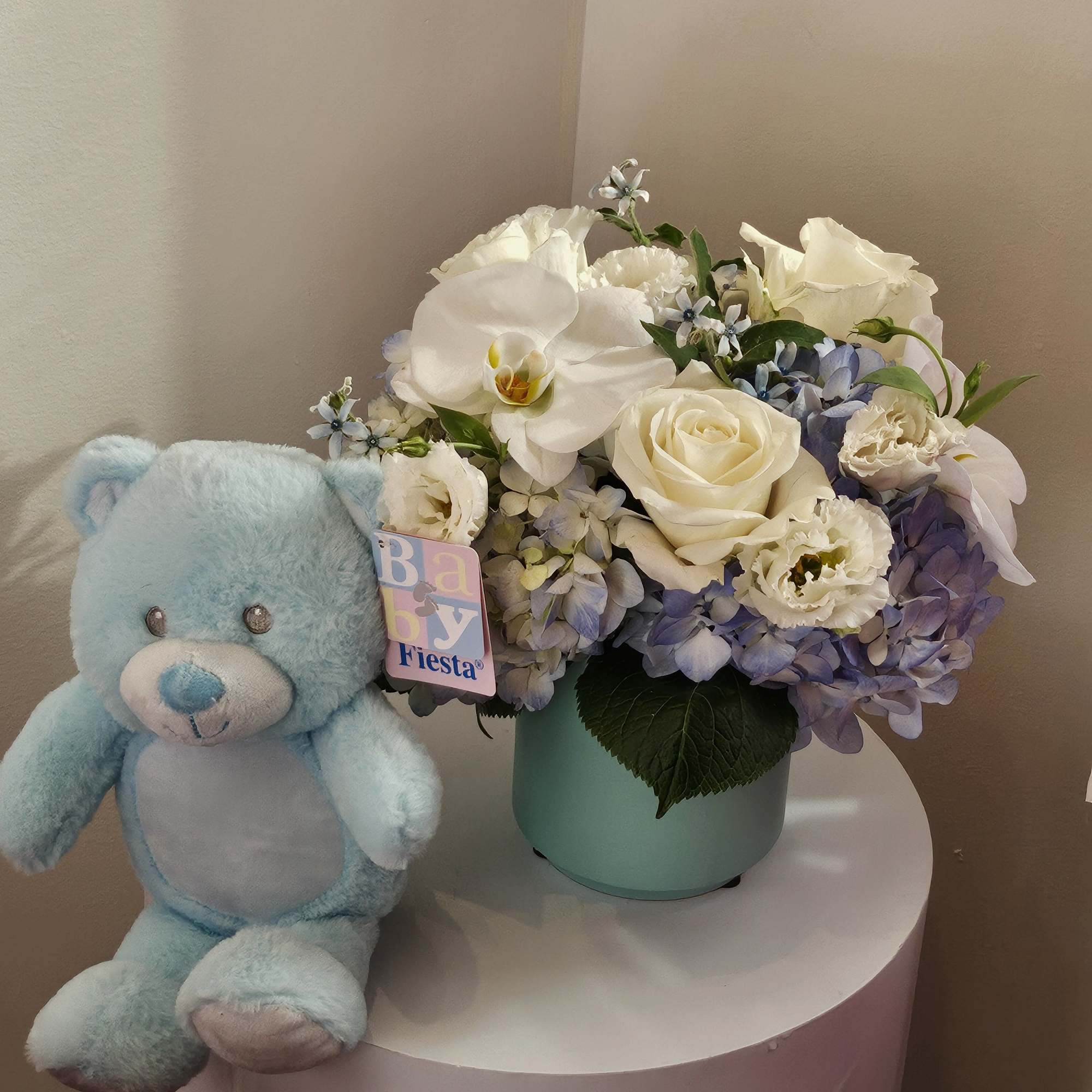 White and lavender flower arrangement in a mint vase beside a blue teddy bear