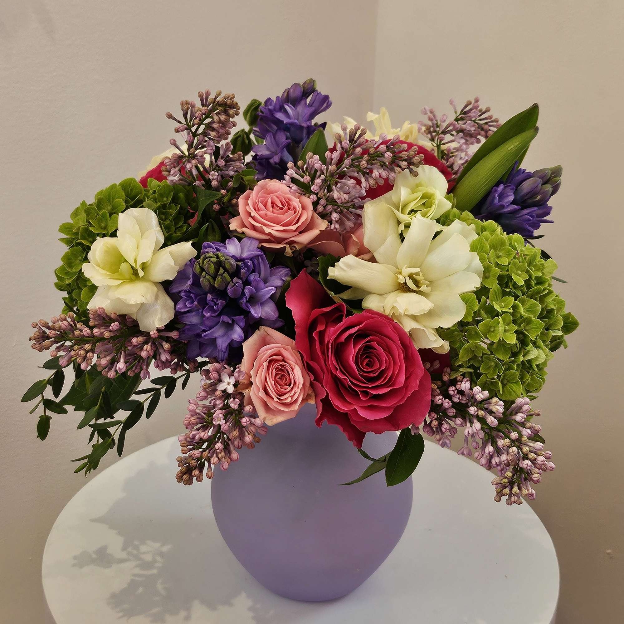 Mixed bouquet of roses, hyacinths, and hydrangeas in a lavender vase