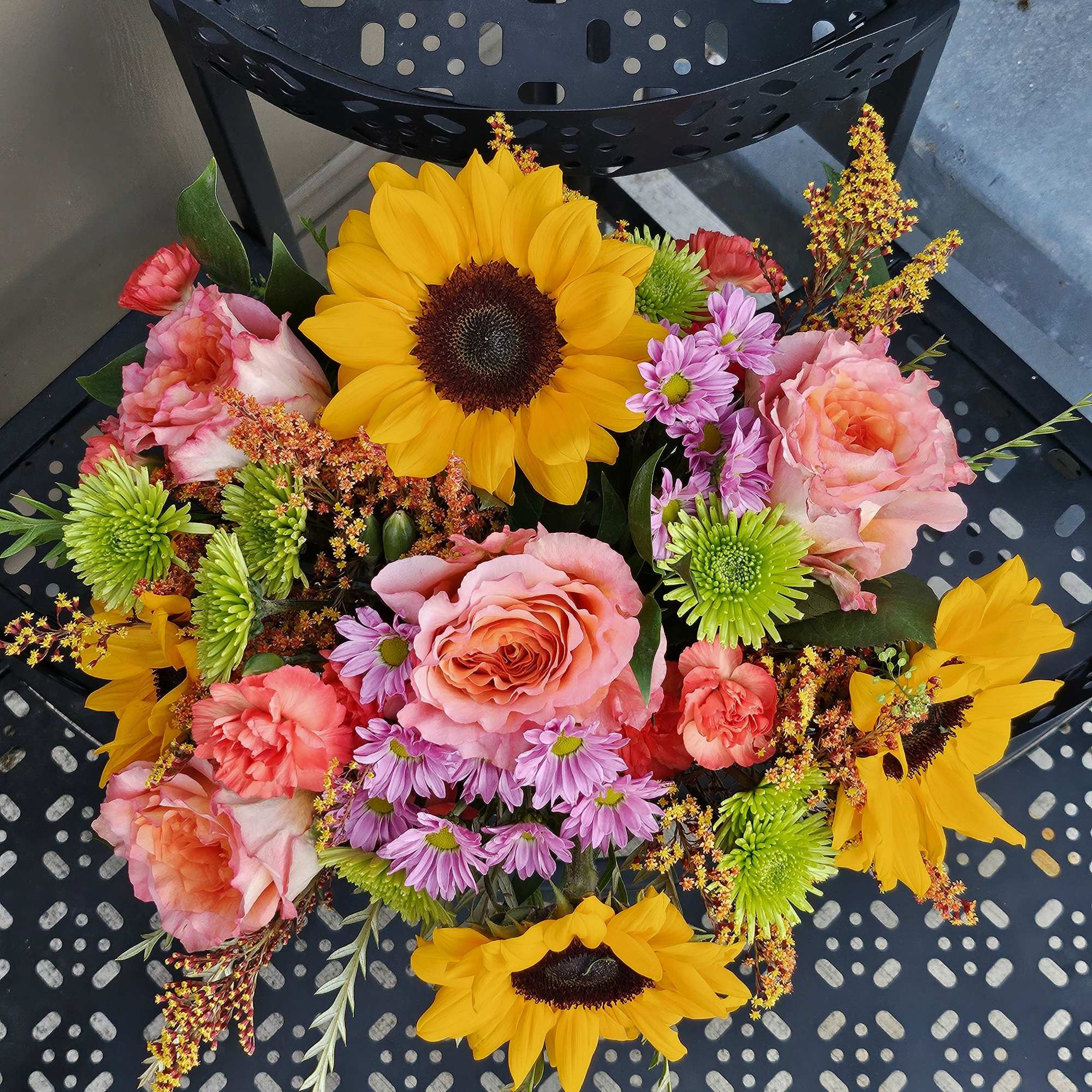 Mixed bouquet with sunflowers, pink roses, and purple daisies in a black container