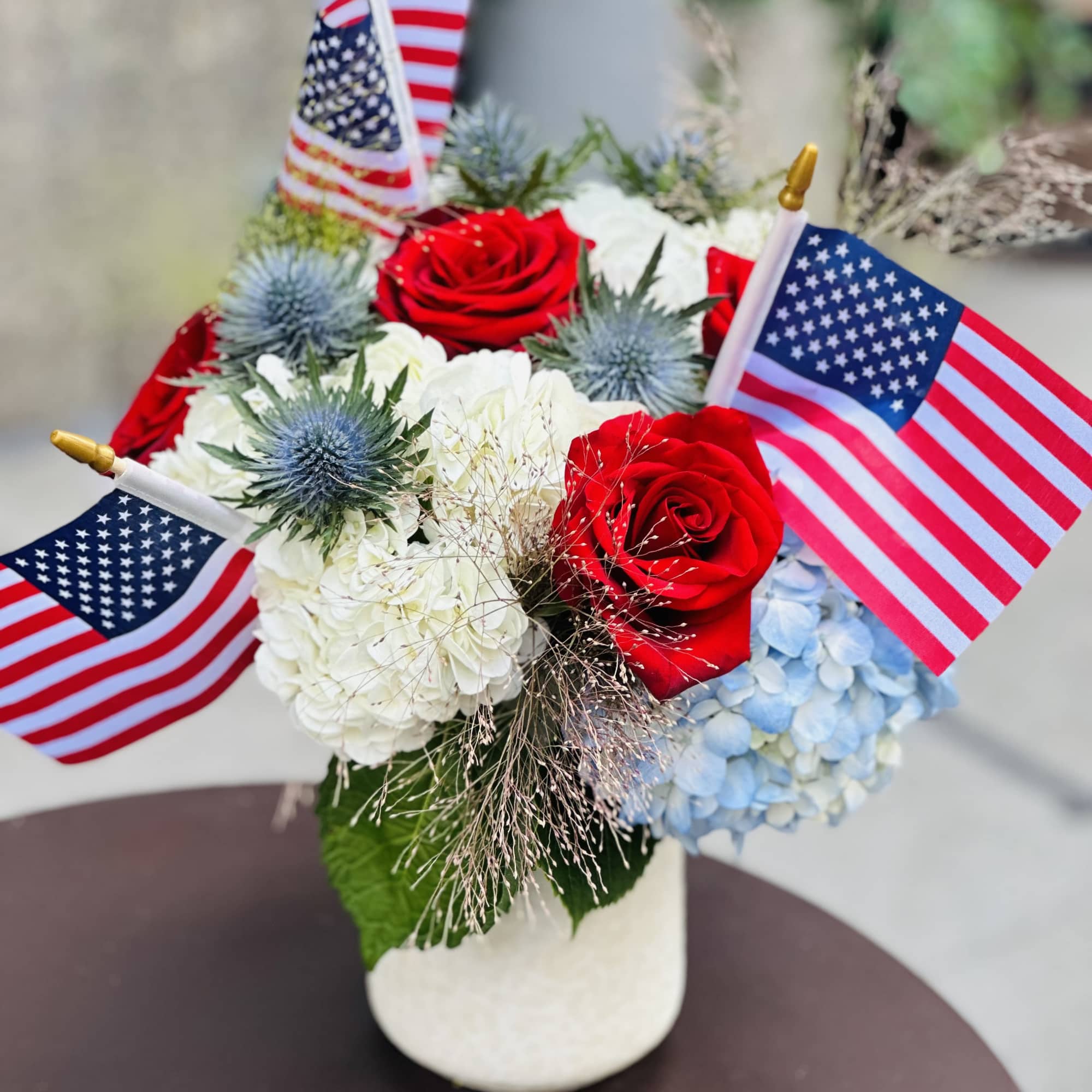 Red roses and hydrangeas in a white vase with small American flags