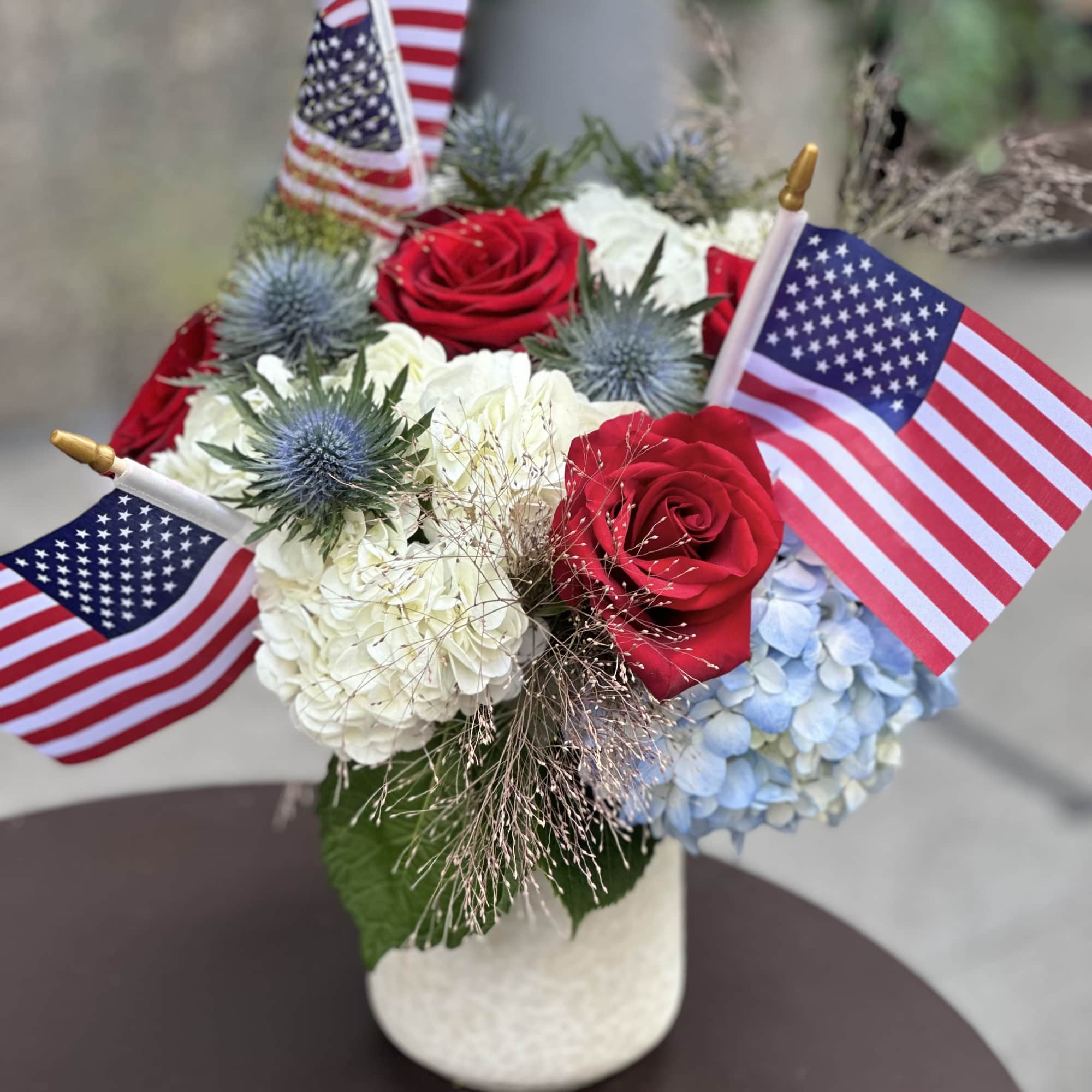 Red roses and hydrangeas in a white vase with small American flags