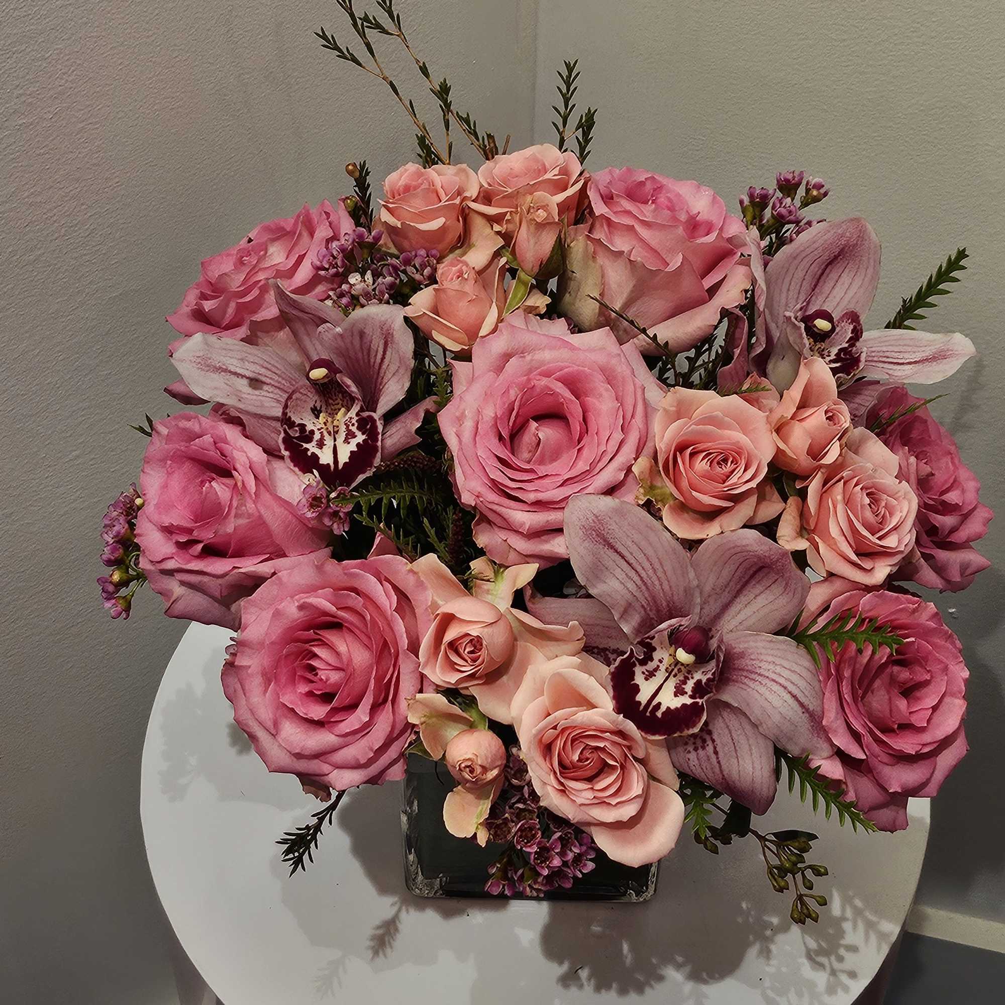 Pink roses and orchids arranged in a square vase