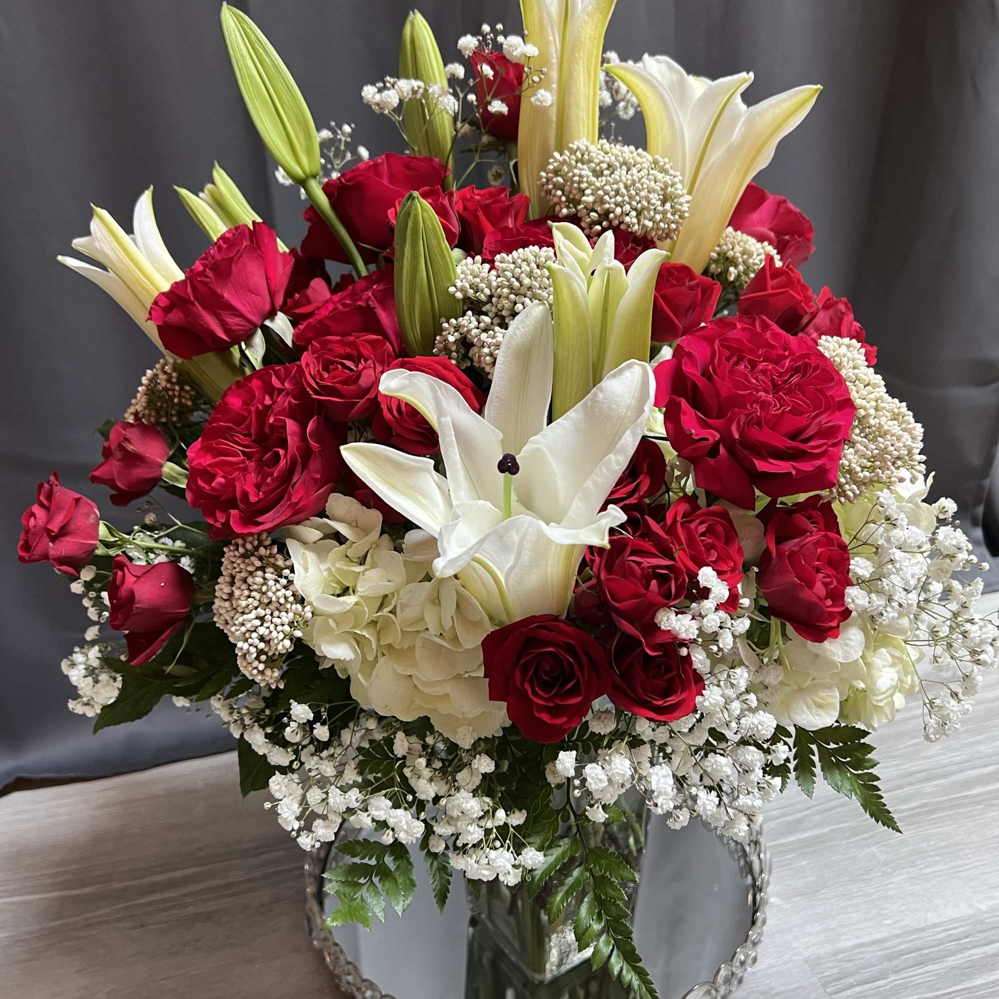 Red roses and white lilies in a mirrored vase with baby's breath