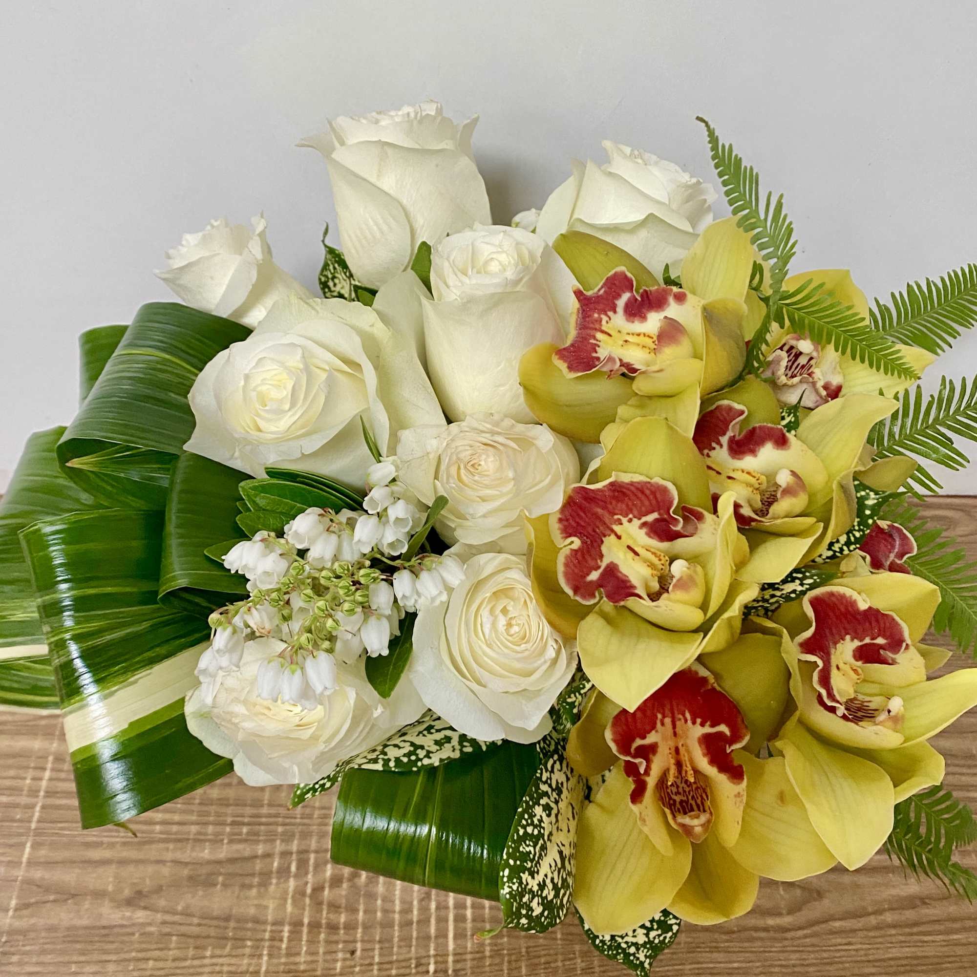 White roses and yellow orchids arranged with tropical leaves
