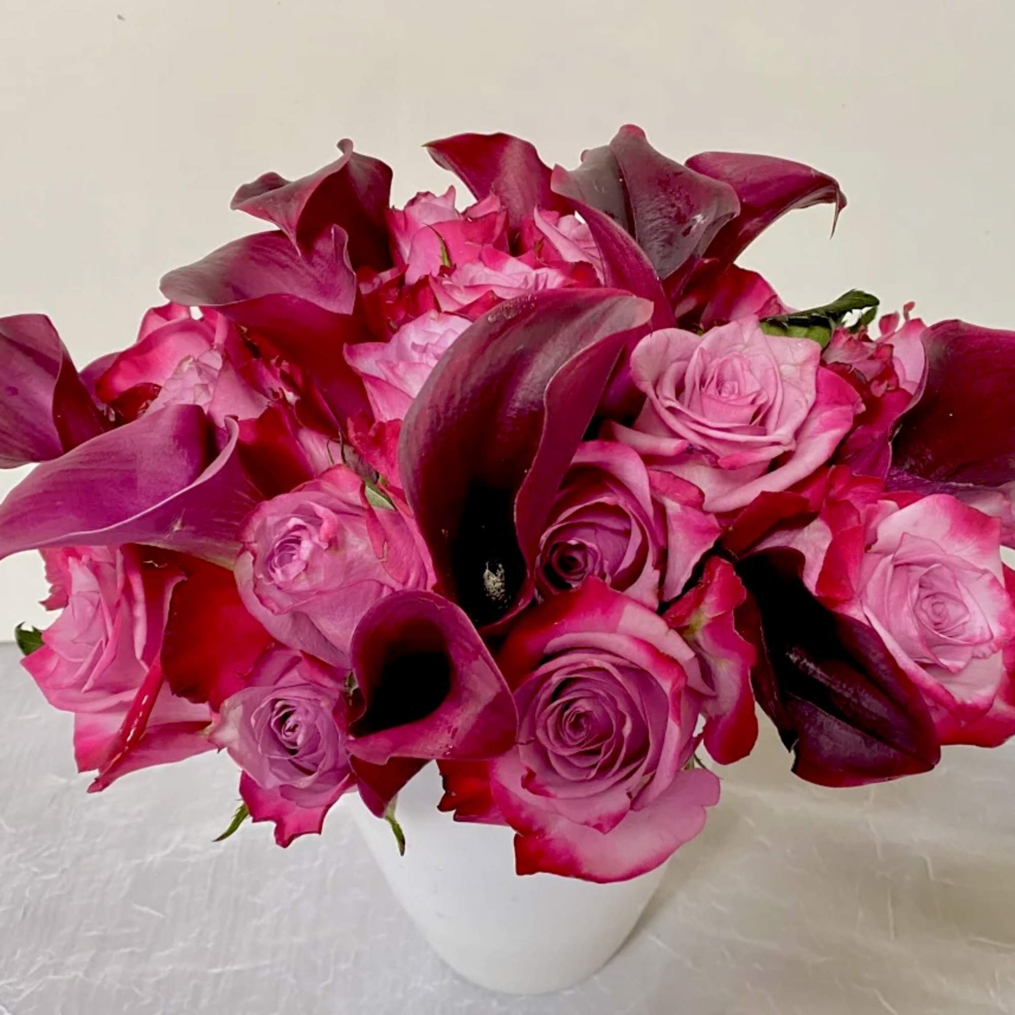 Pink roses and dark magenta calla lilies in a white vase