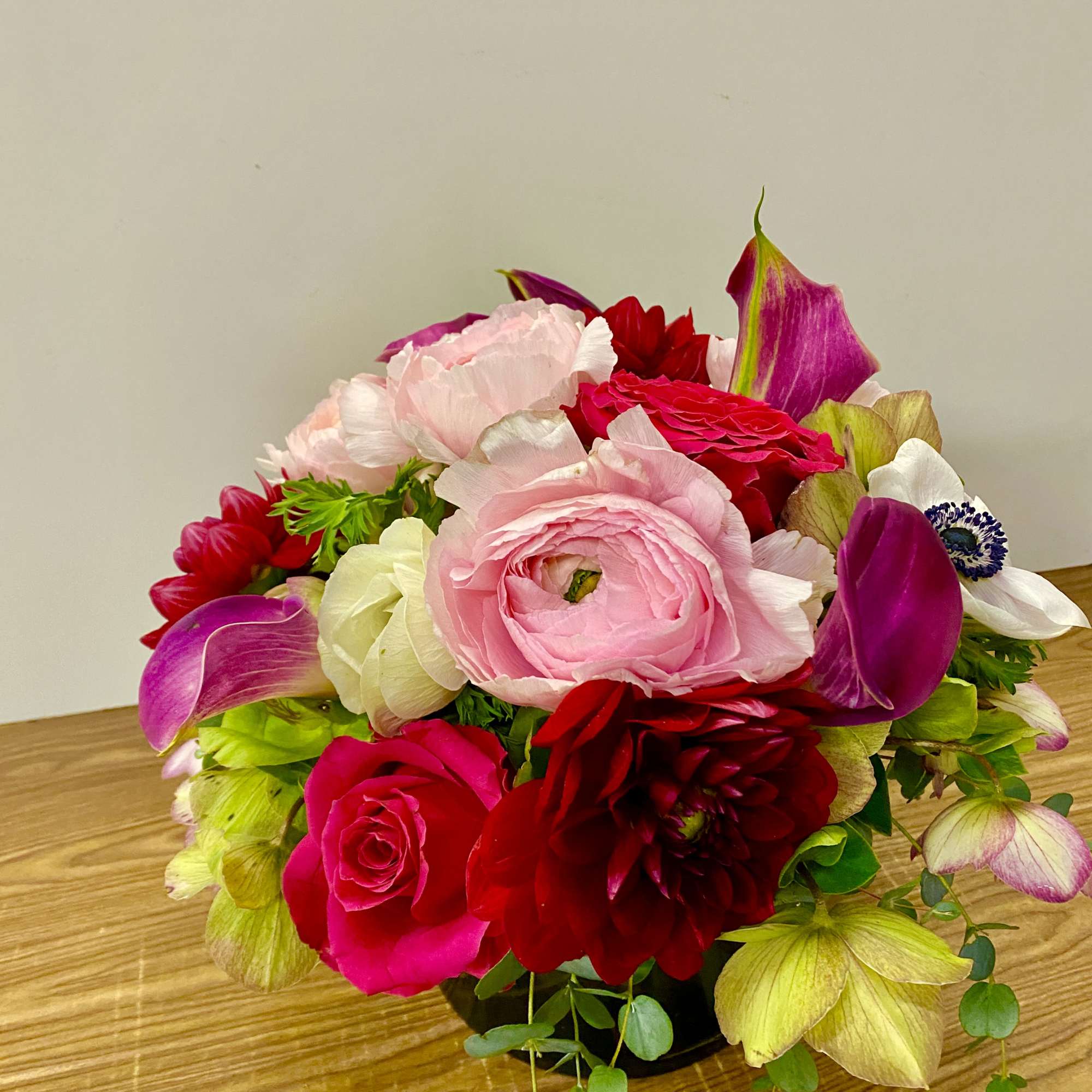 Low arrangement of pink and red blooms with white accents in a black vase on a wooden surface