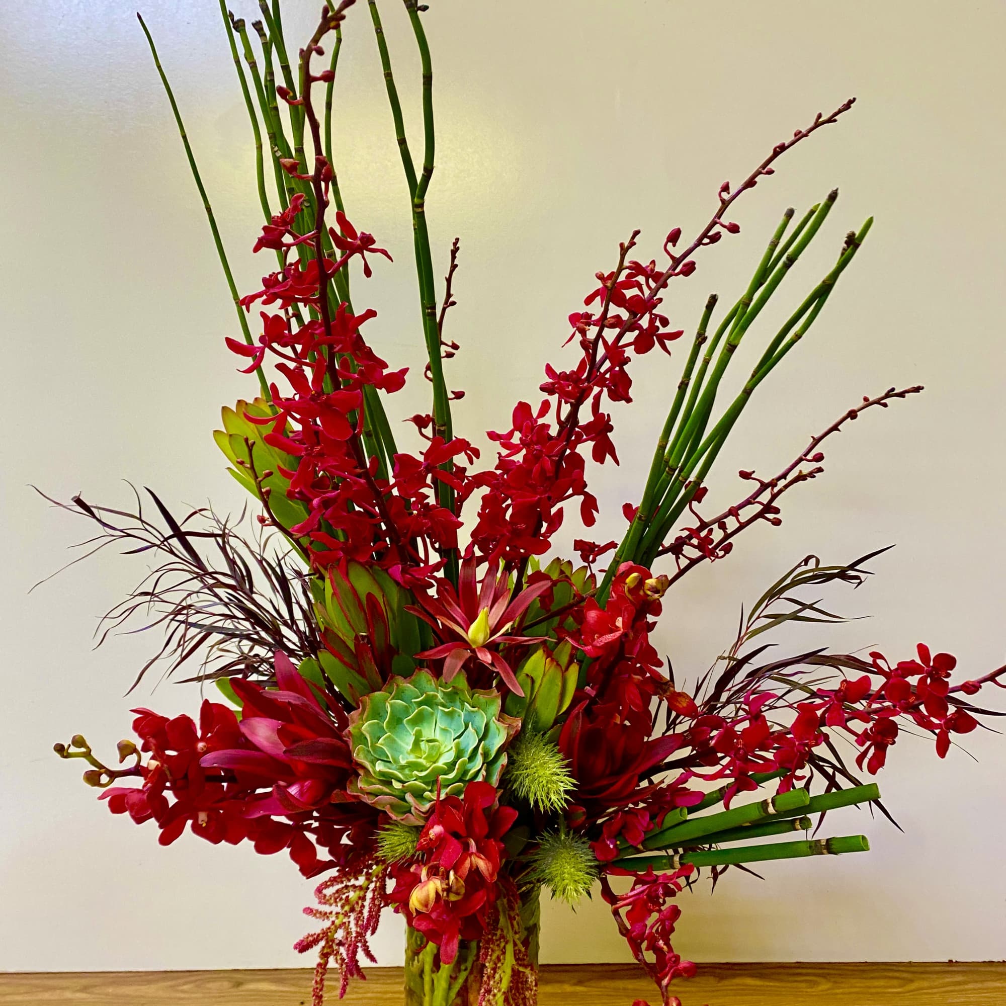 Tall red orchid arrangement in a glass vase with green succulent accents