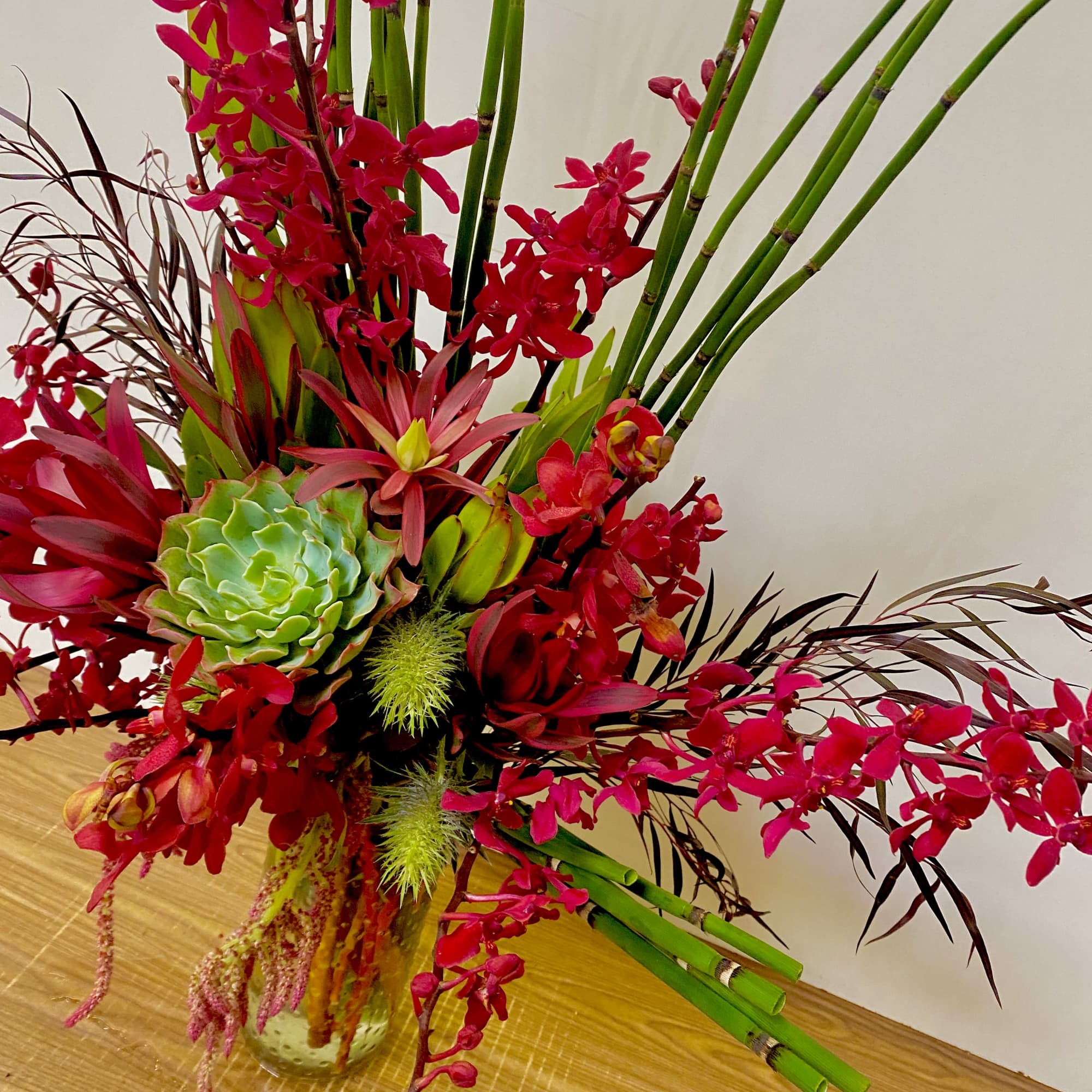 Tropical floral arrangement with red orchids and a green succulent in a vase