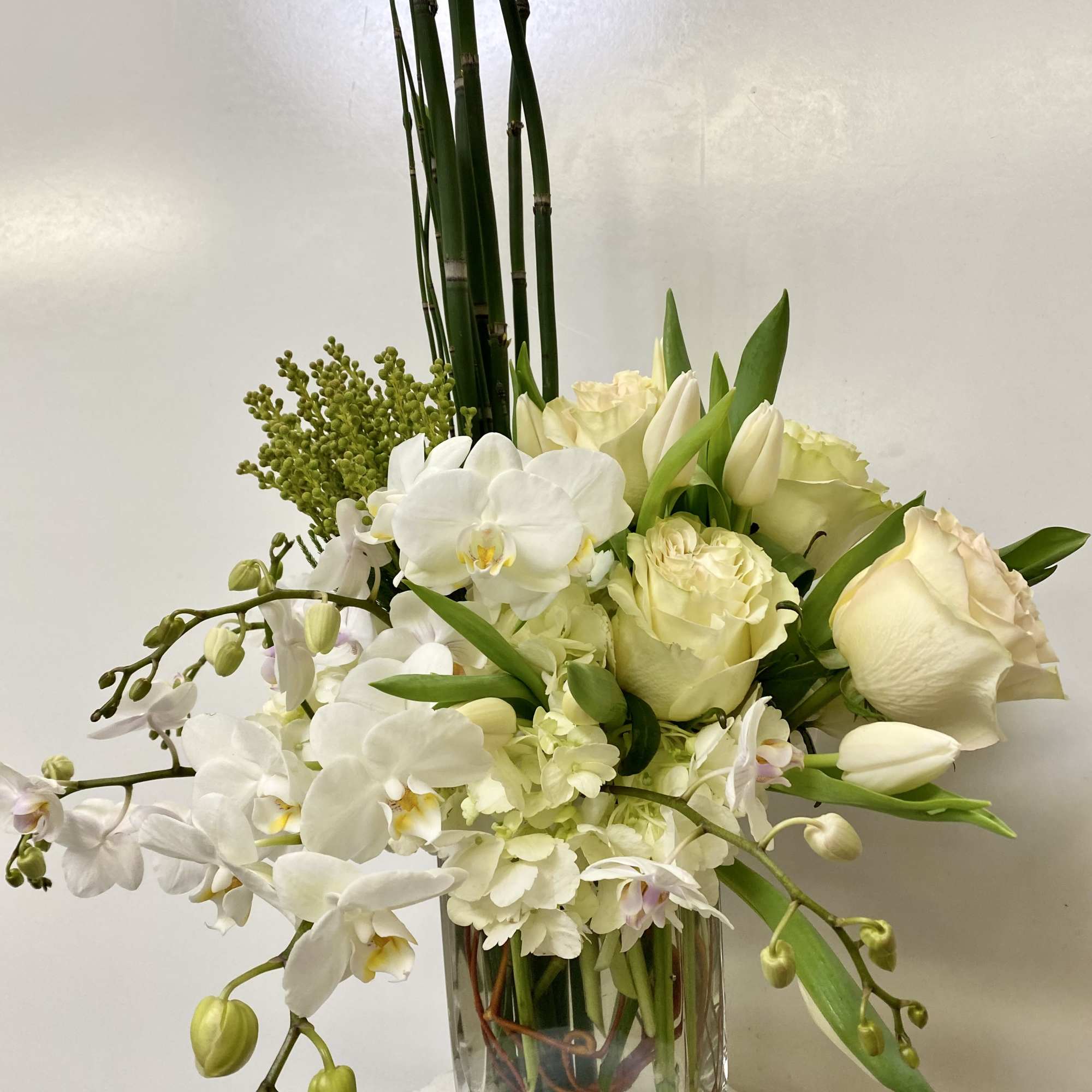 White orchids and roses arranged in a clear glass vase