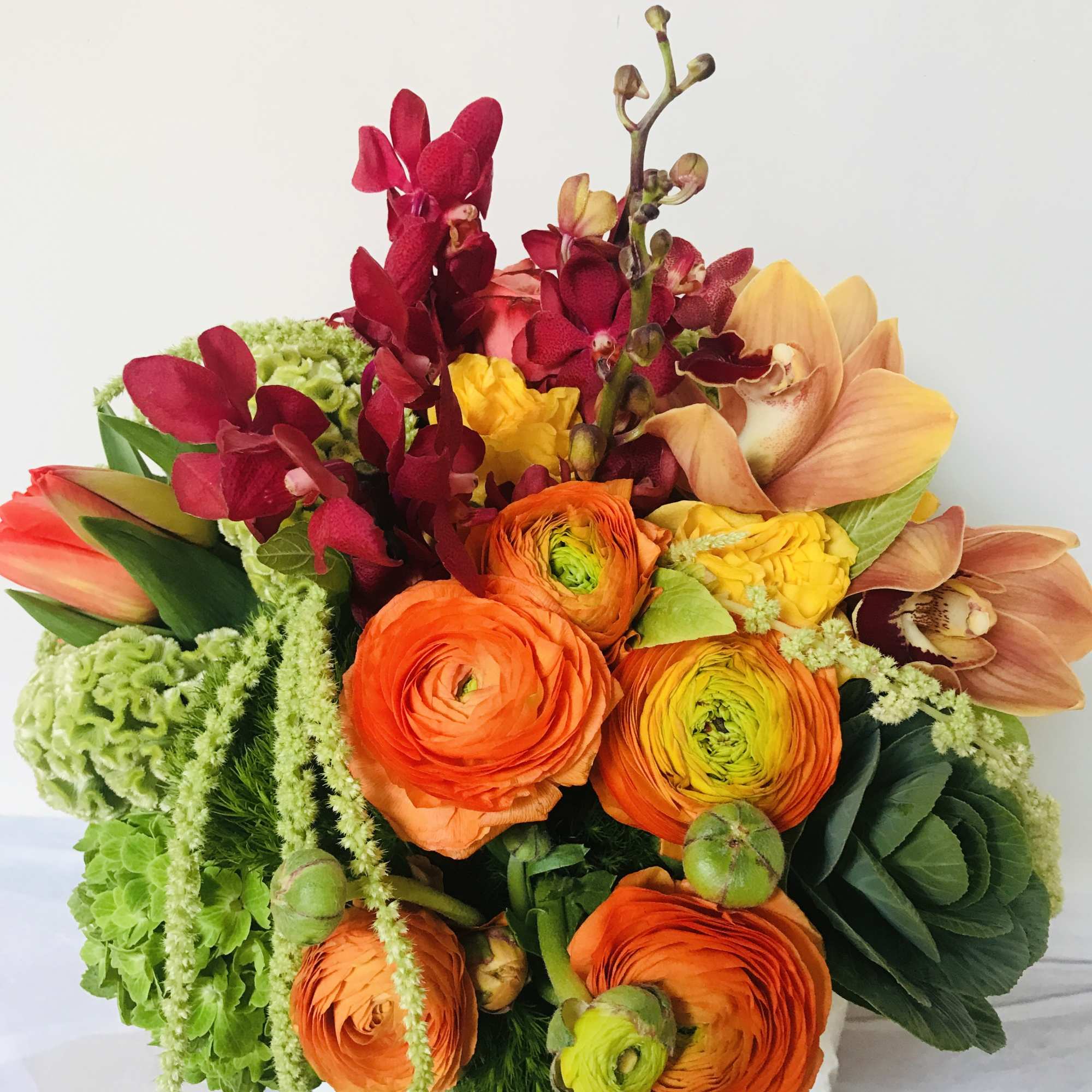 Bright bouquet of orange ranunculus and orchids in a vase