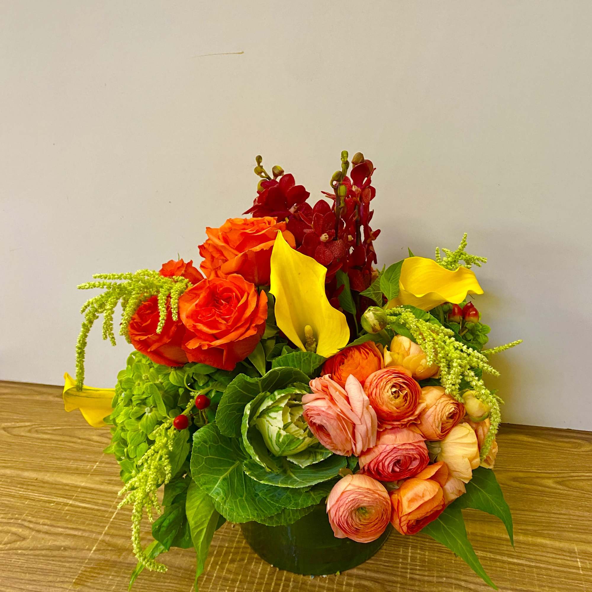 Bright mixed floral arrangement with roses, calla lilies, and red orchids in a low container