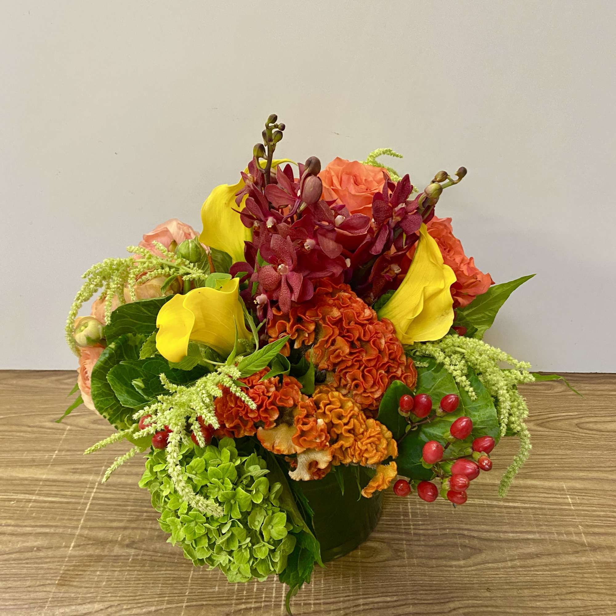 Bright mixed bouquet with yellow calla lilies, orange blooms, and green hydrangea in a vase