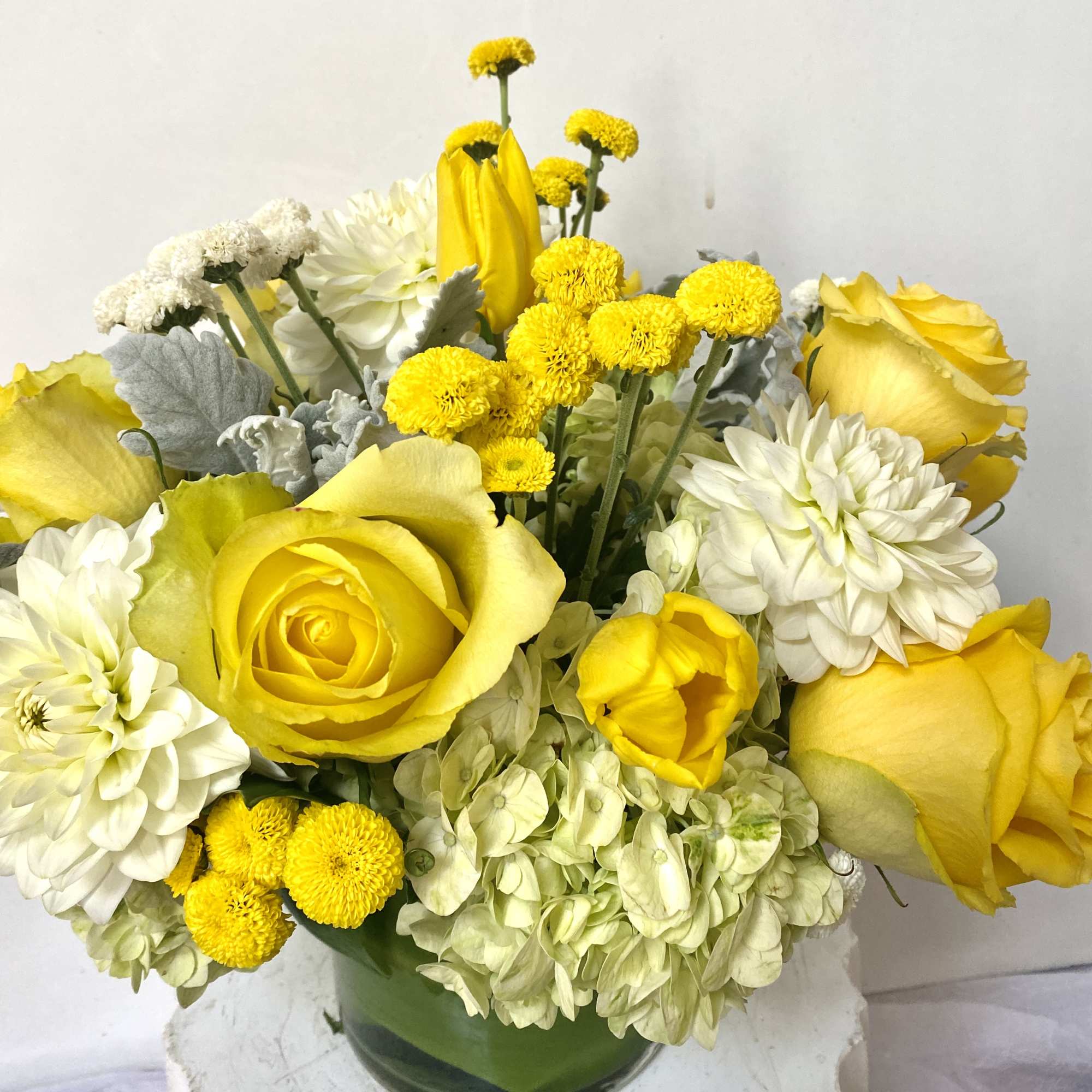 Yellow roses and white blooms arranged in a glass vase