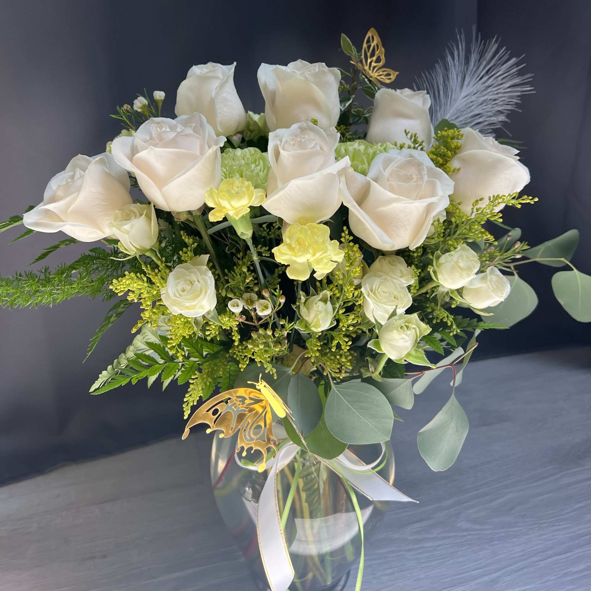 White rose bouquet in a glass vase with green accents and butterfly decorations