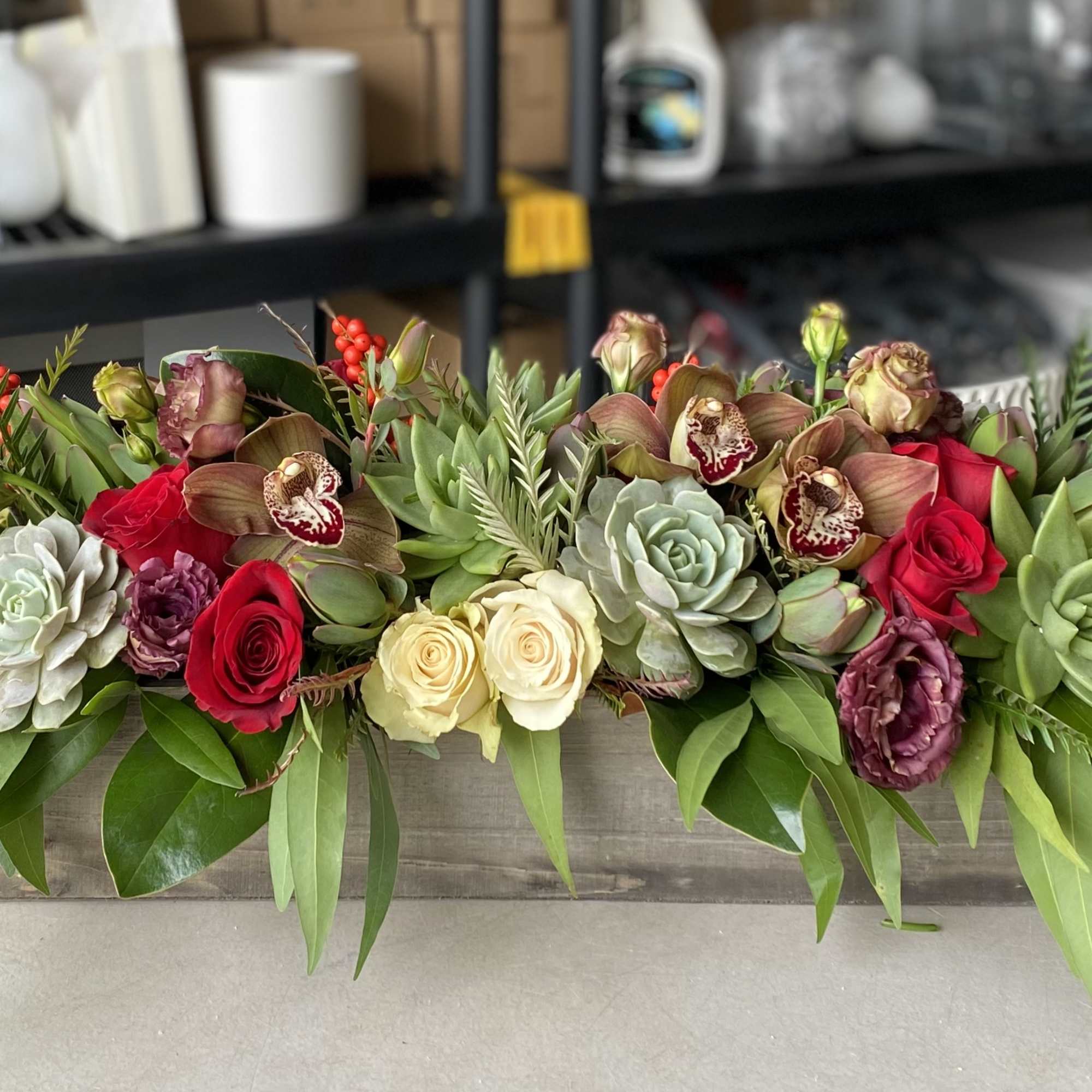 Long floral centerpiece with roses, orchids, and succulents in a low container