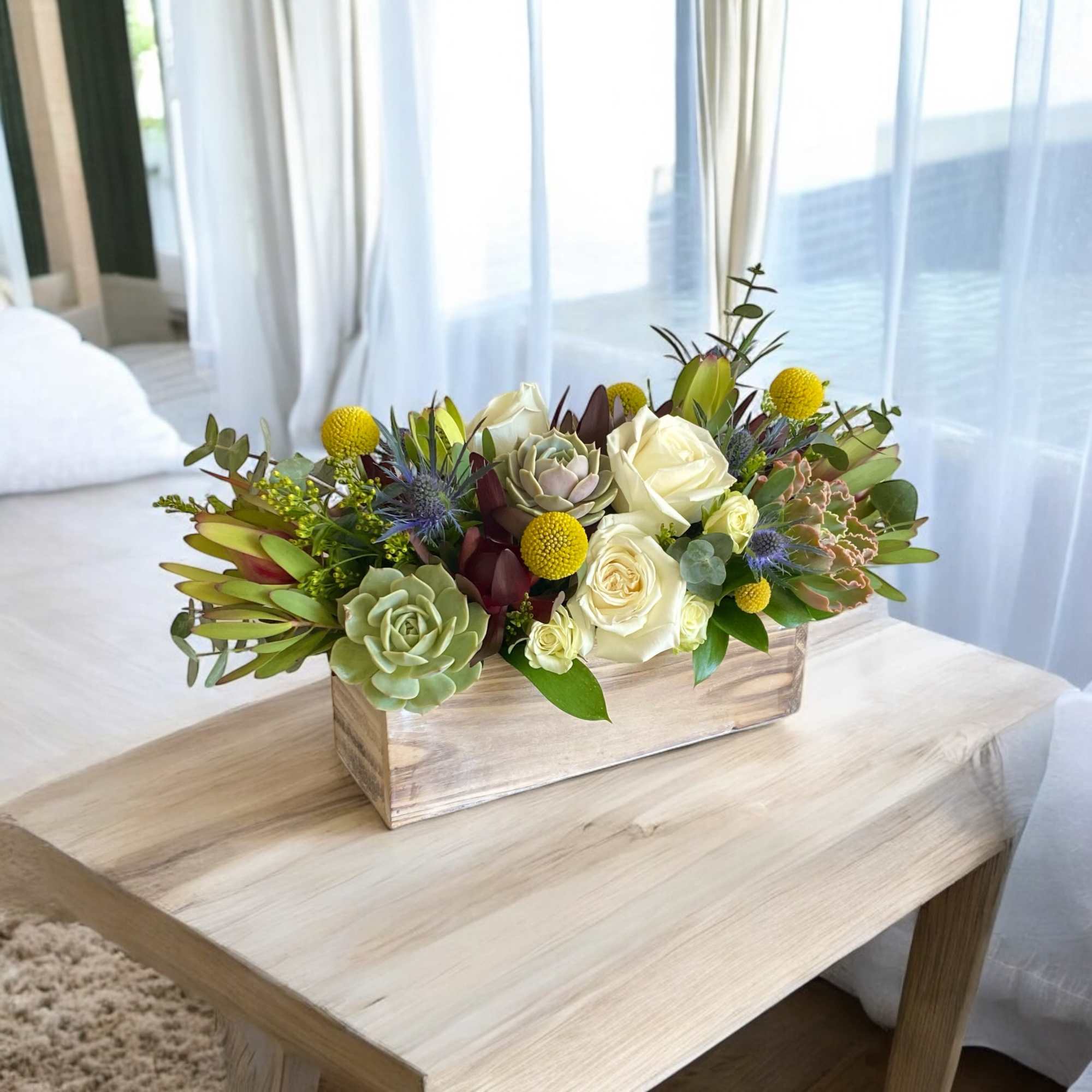 Low floral arrangement in a wooden box with white roses and succulents