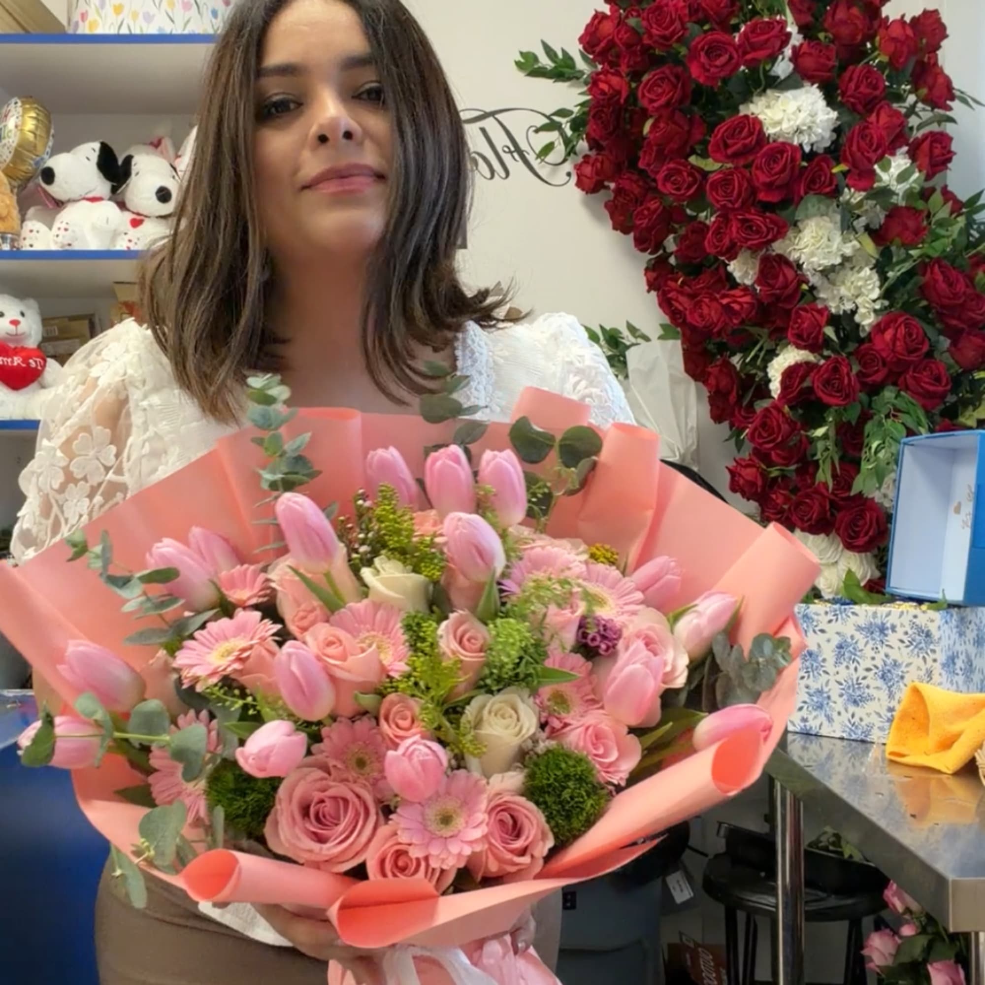 Woman holding a pink bouquet of roses, tulips, and daisies wrapped in peach paper
