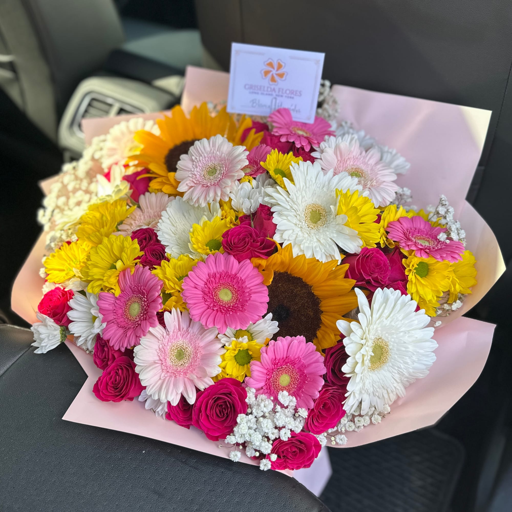 Mixed bouquet of gerbera daisies, sunflowers, and pink roses wrapped in pale pink paper