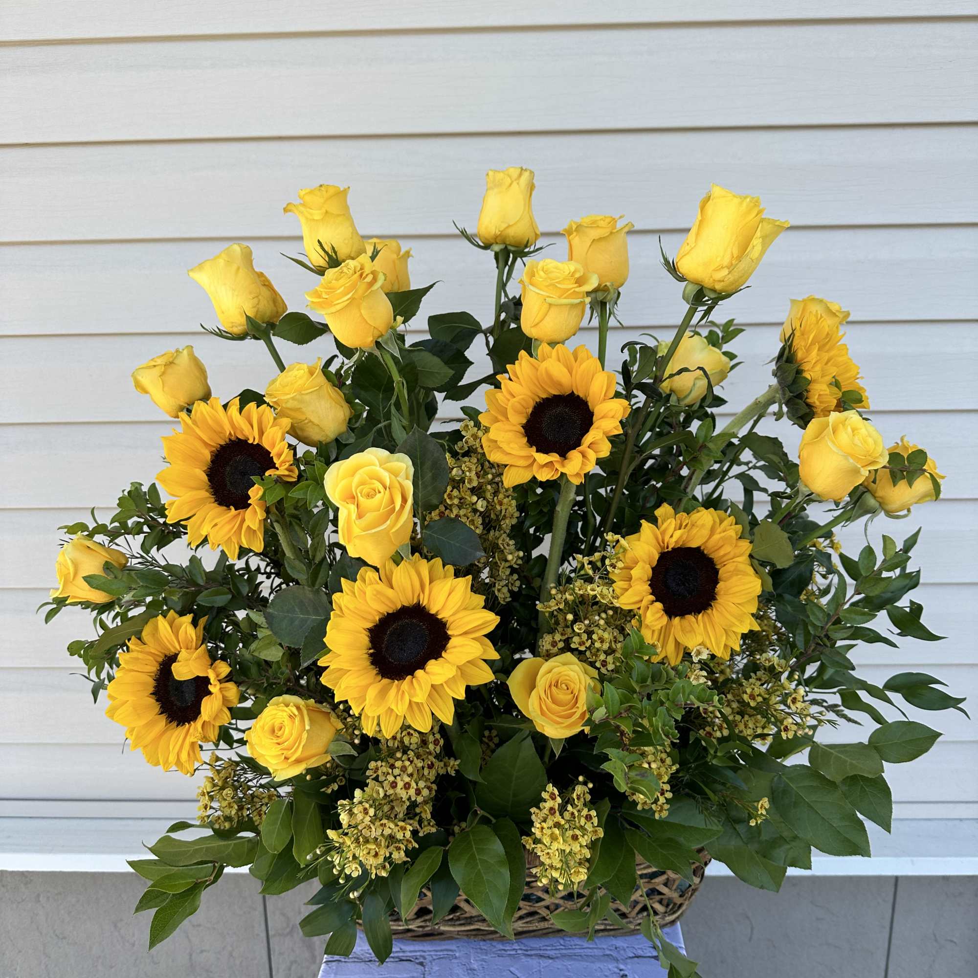 Yellow roses and sunflowers arranged in a wicker basket