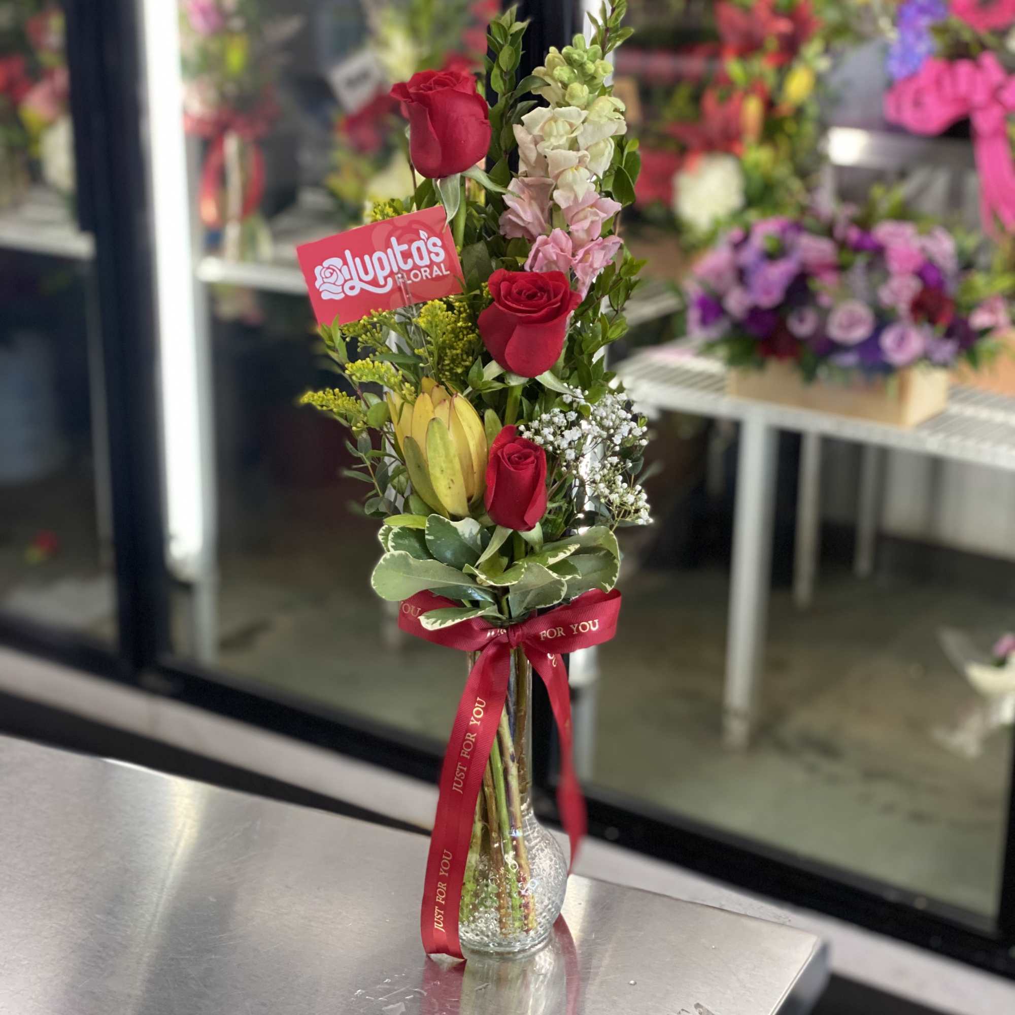 Tall bouquet of red roses and mixed flowers in a clear glass vase